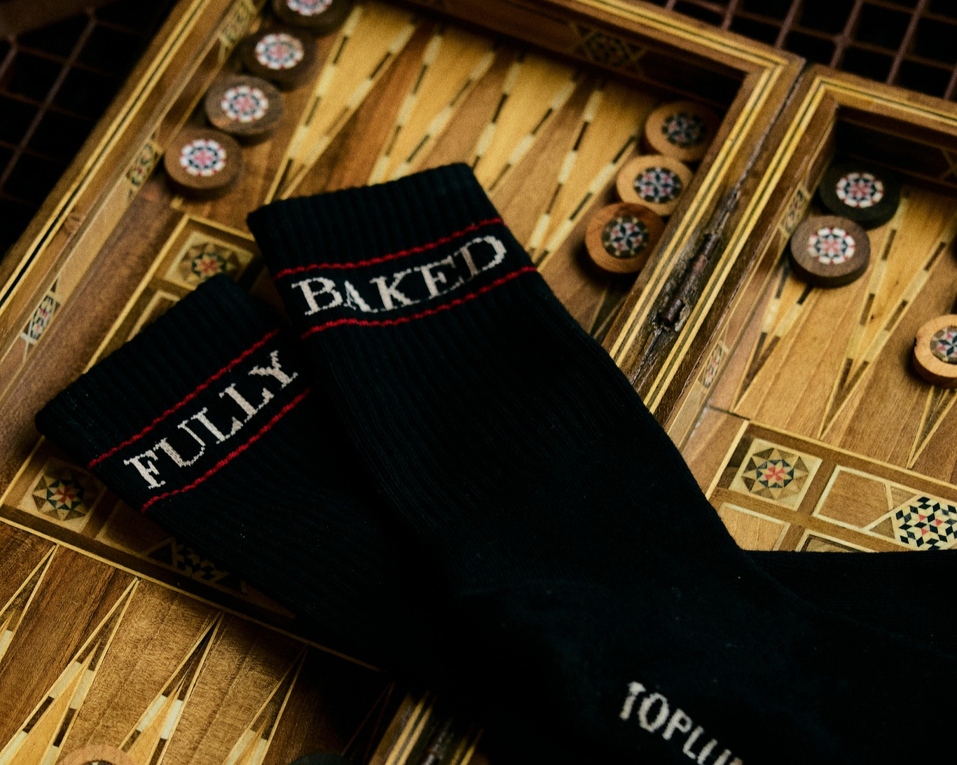 Black socks with red and white text that reads 'FUTURE' and 'BAKED' on a decorative chessboard.