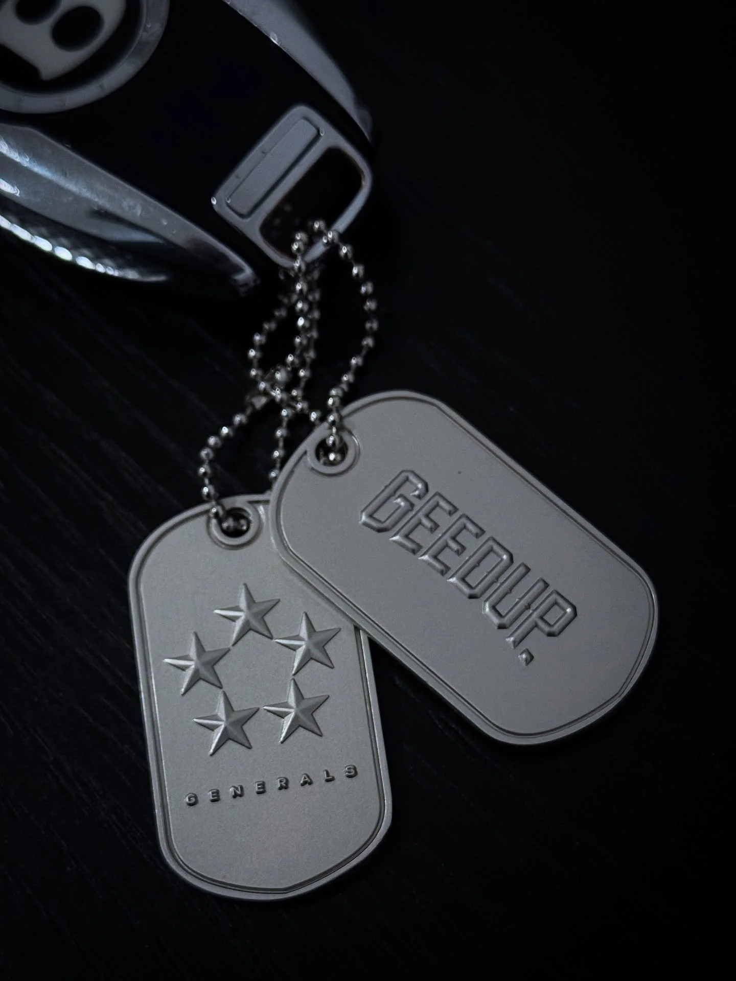 Close-up of two metallic dog tags attached to a ball chain, one with five stars and the other with the word 'GEOUP' and three stars.