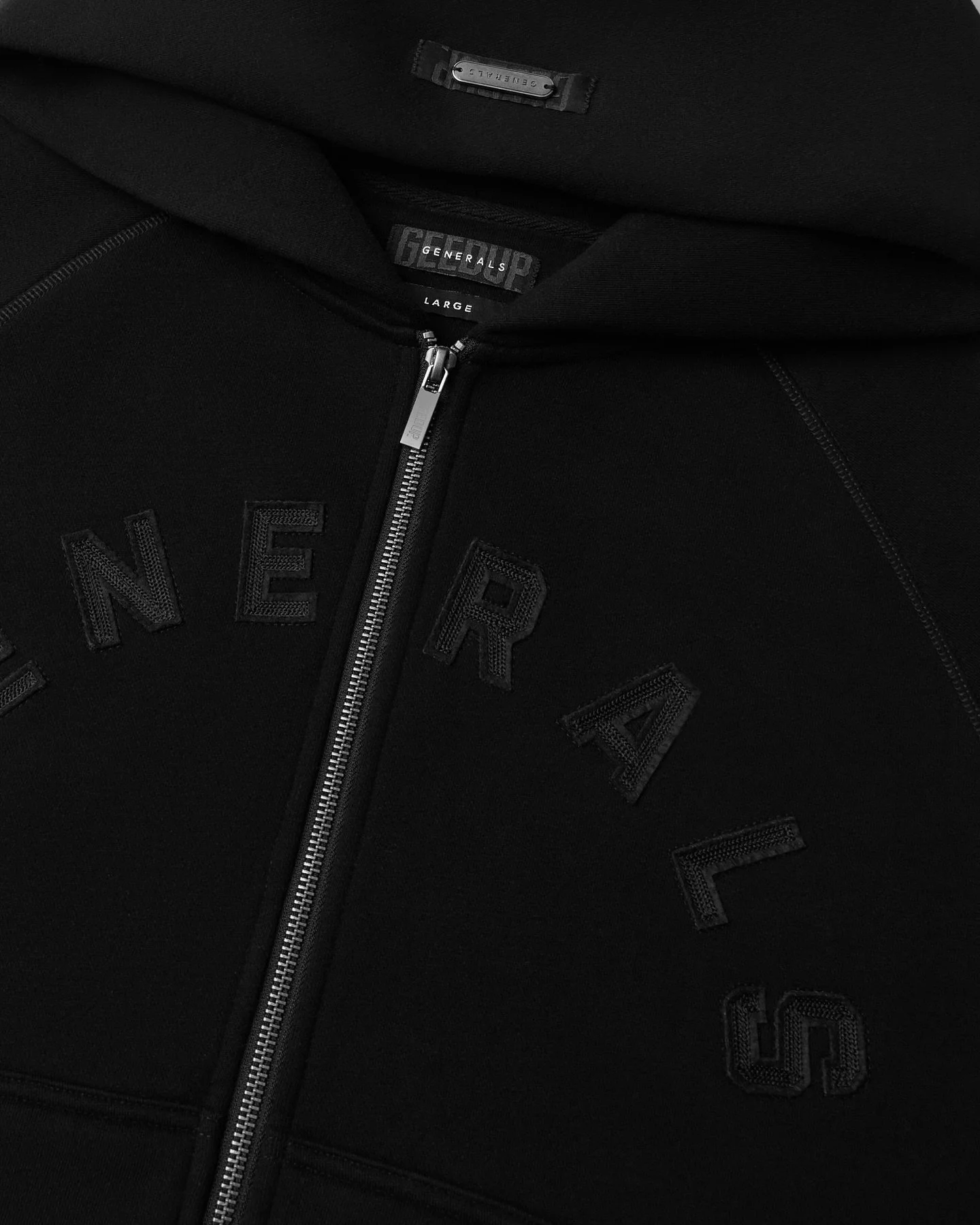 Close-up of a black hoodie with a silver zipper, black embroidered letters spelling 'NERD', and a small fabric tag inside the collar reading 'Generals Large'.