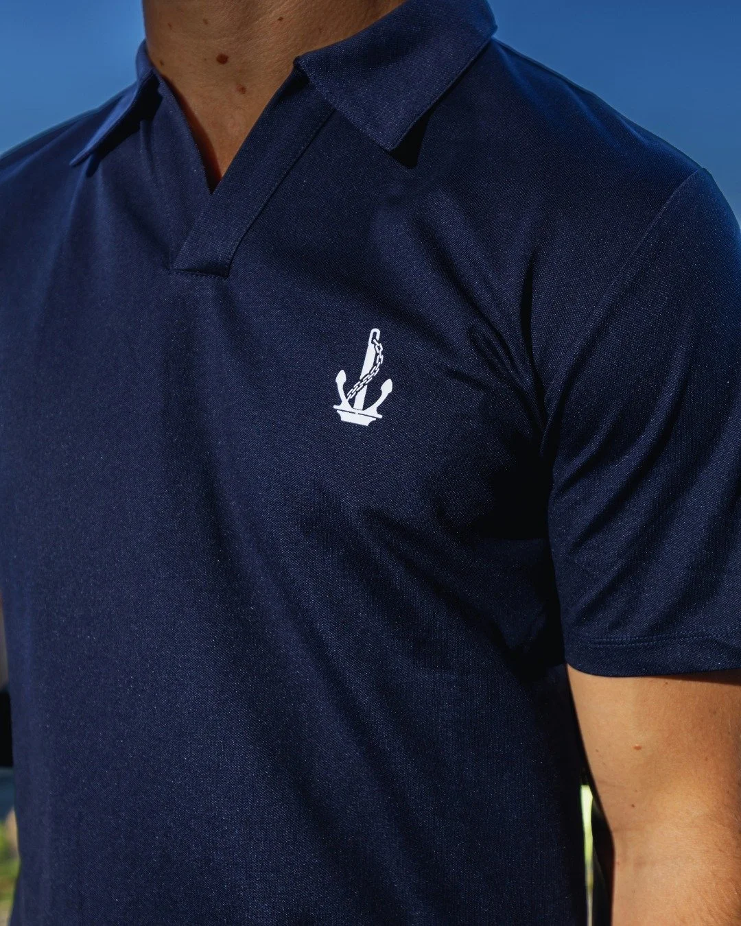 Close-up of a person wearing a navy blue polo shirt with a small white logo of an anchor with a chain on the chest.
