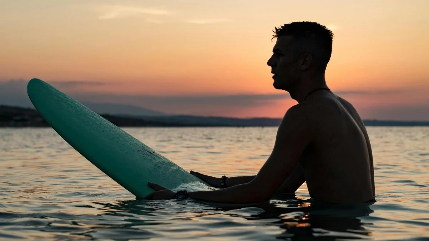 Surfer sitting on a surfboard at sunset during a surf session in Lombok.