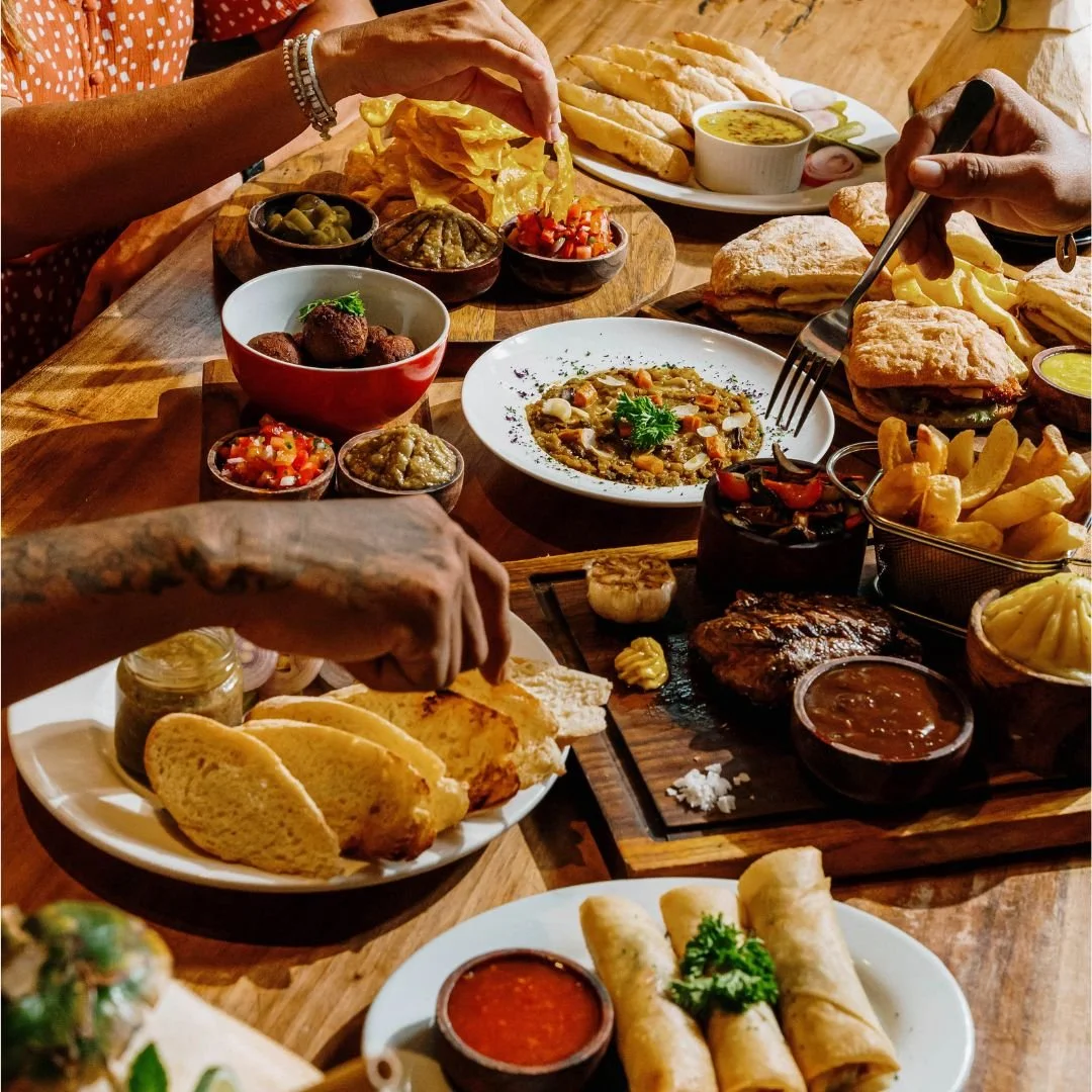 A table filled with various dishes of Tenderloin Steak, Lentil Curry, Chickpea Falafels, Spring Rolls, Nachos, Chicken Sandwich and Duck Rilette at Treehouse Restaurant and Bar in Kuta Lombok