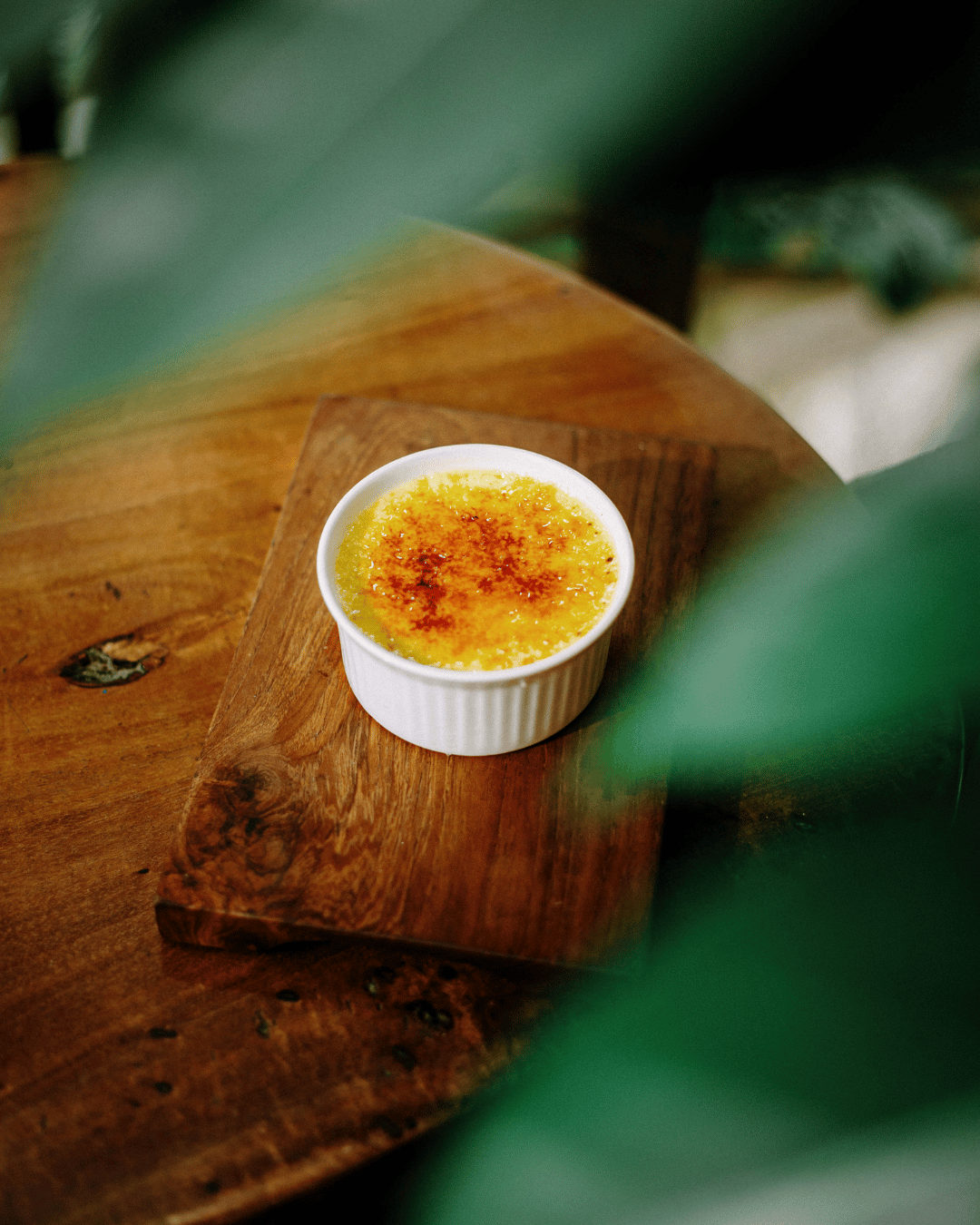 A small ramekin of crème brûlée with caramelized sugar topping on a wooden tray at Treehouse Restaurant in Kuta Lombok.