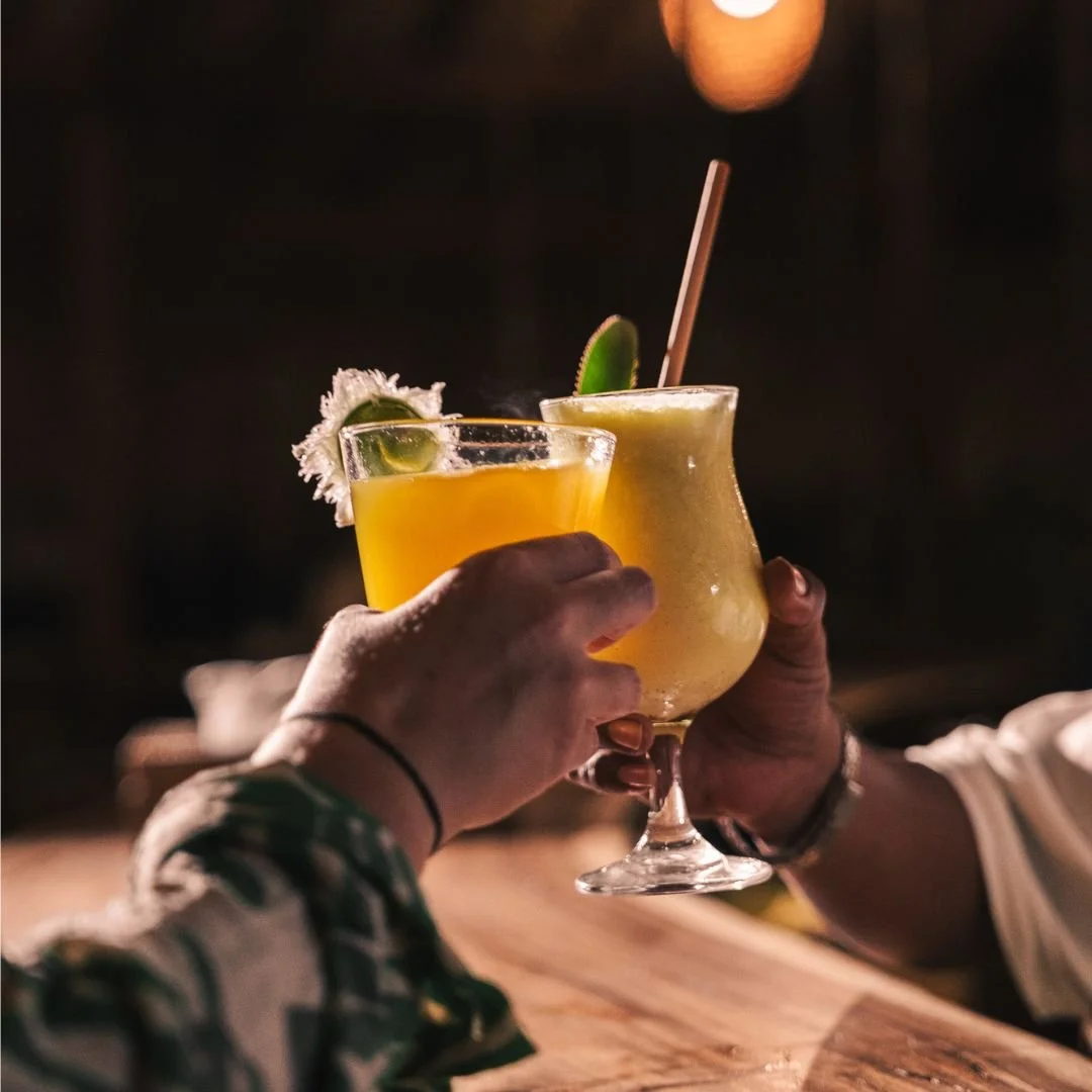 Two people clinking tropical cocktails with lime garnish in a dark setting.