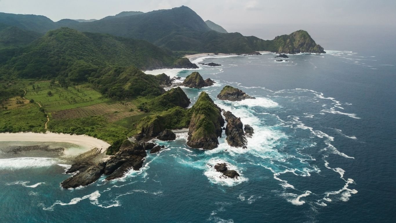 Aerial view of Mawi Beach featuring rugged cliffs, white sand and waves on Lombok's south coast.