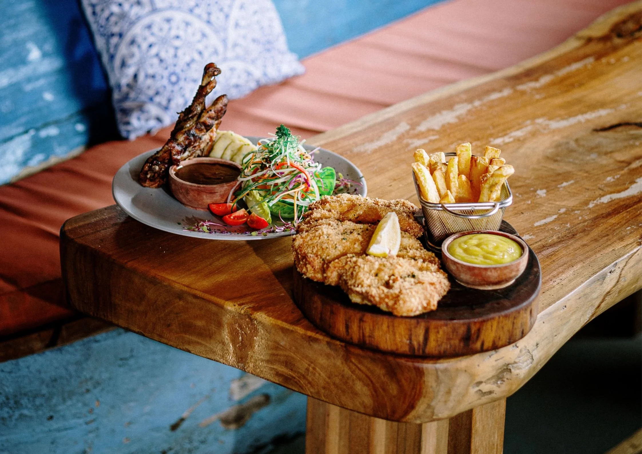 Plate of Chicken Schnitzel, salad, Duck Leg, fries, and dipping sauces on a wooden table at Treehouse in Kuta Lombok.