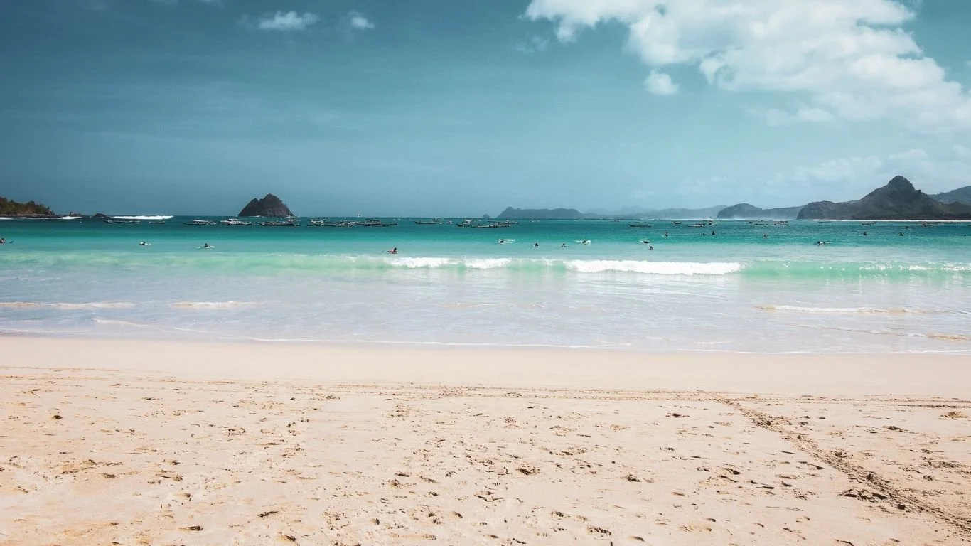 Selong Belanak Beach with white sand, clear water and surfers enjoying the waves in Lombok.