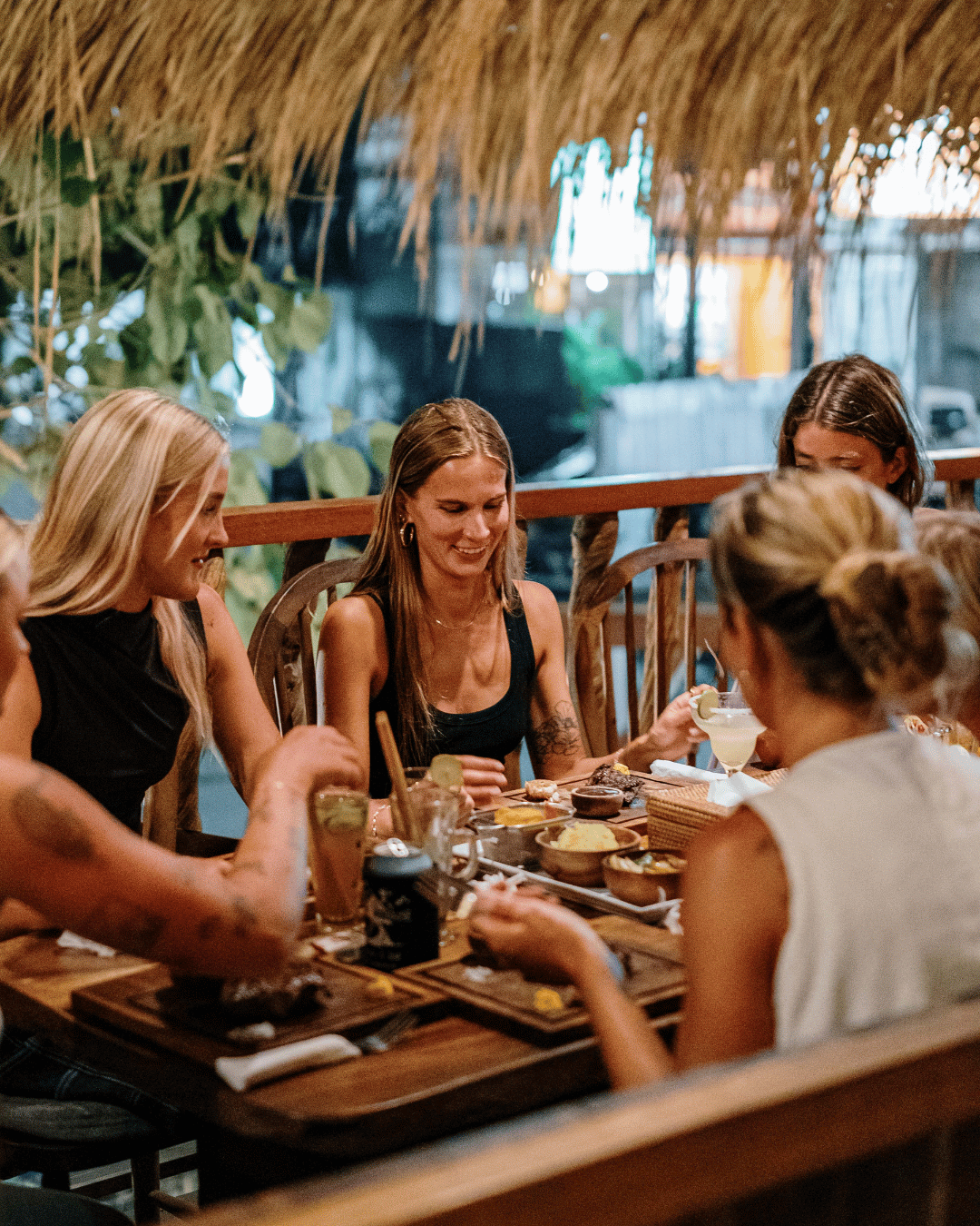 Women enjoying a meal at Treehouse restaurant with a tropical-themed decor, including thatched roof ceiling and potted plants.