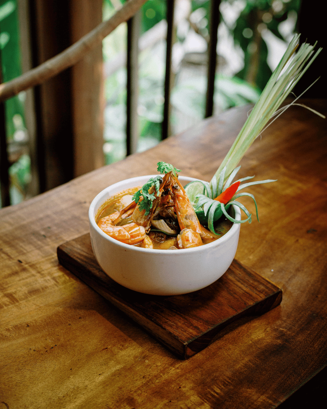 Freshly prepared lunch of Thai Tom Yum seafood soup, garnished with herbs, on a wooden table at Treehouse Restaurant