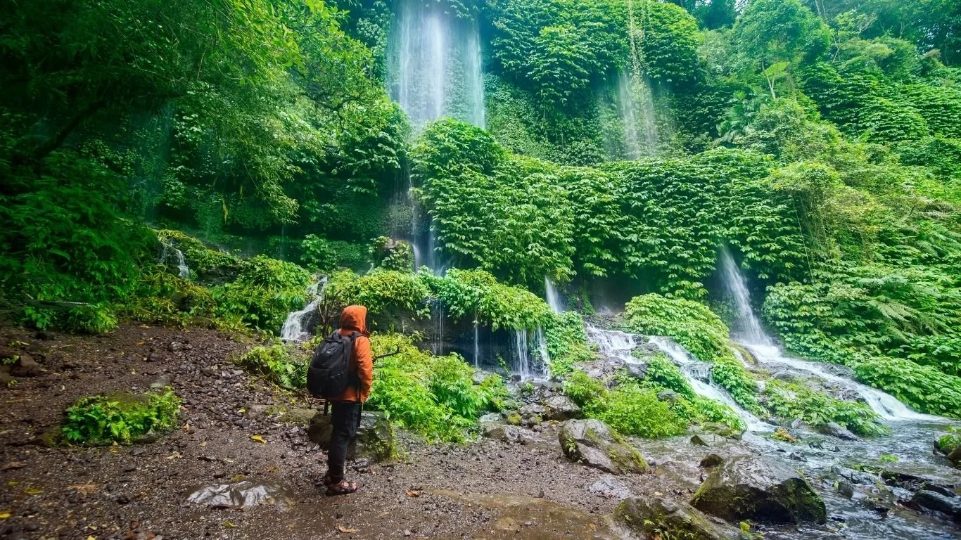 Traveller standing in front of Benang Kelambu Waterfall surrounded by lush tropical forest in Lombok.