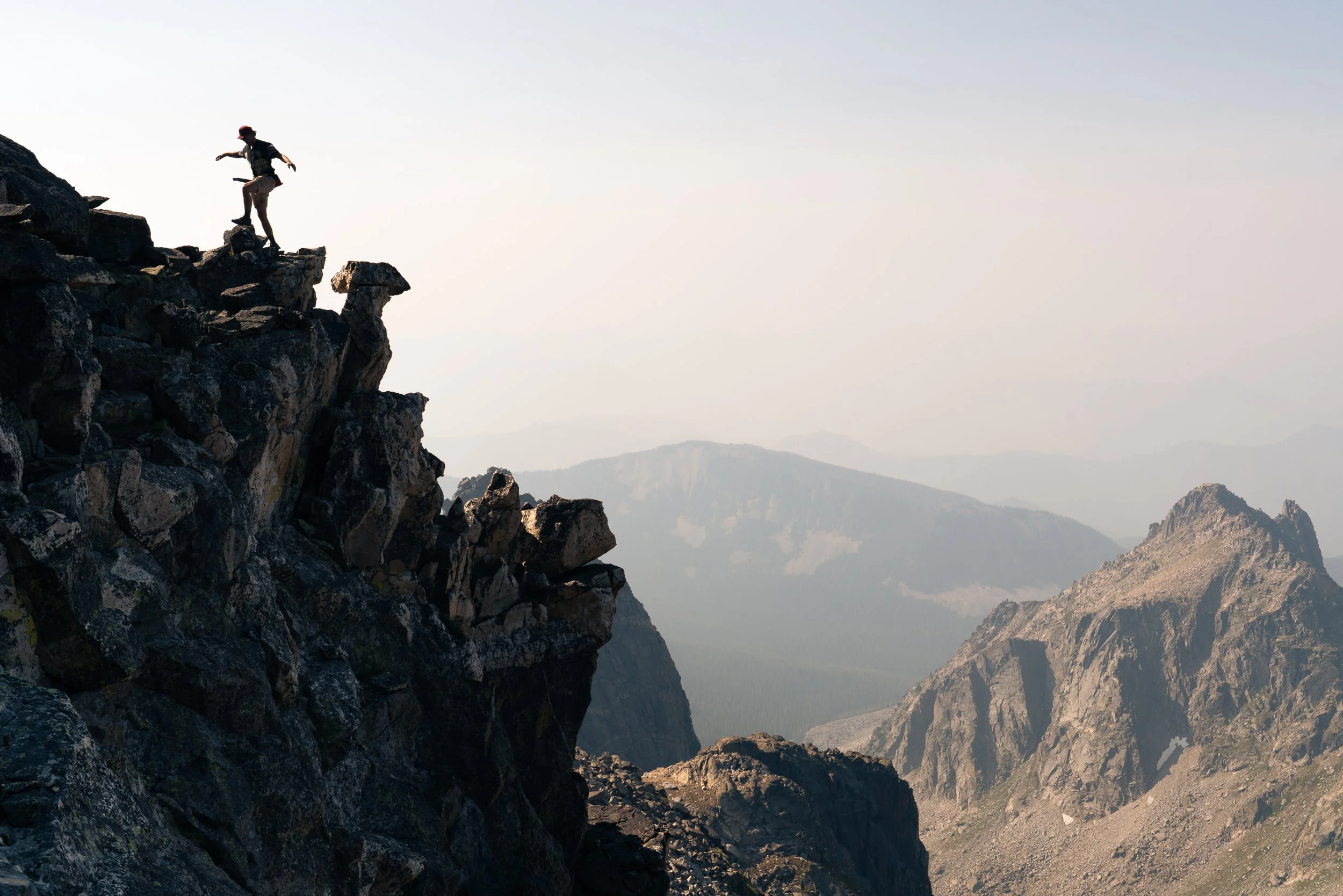 Person standing on a rocky mountain ridge with mountains in the background.
