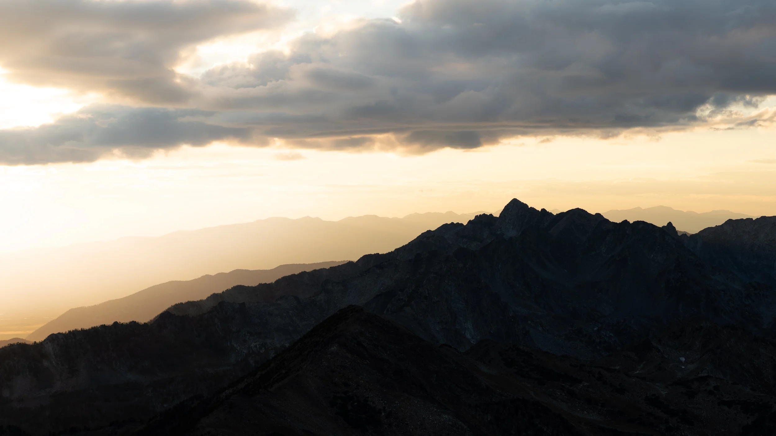 Mountain range at sunset with cloudy sky.