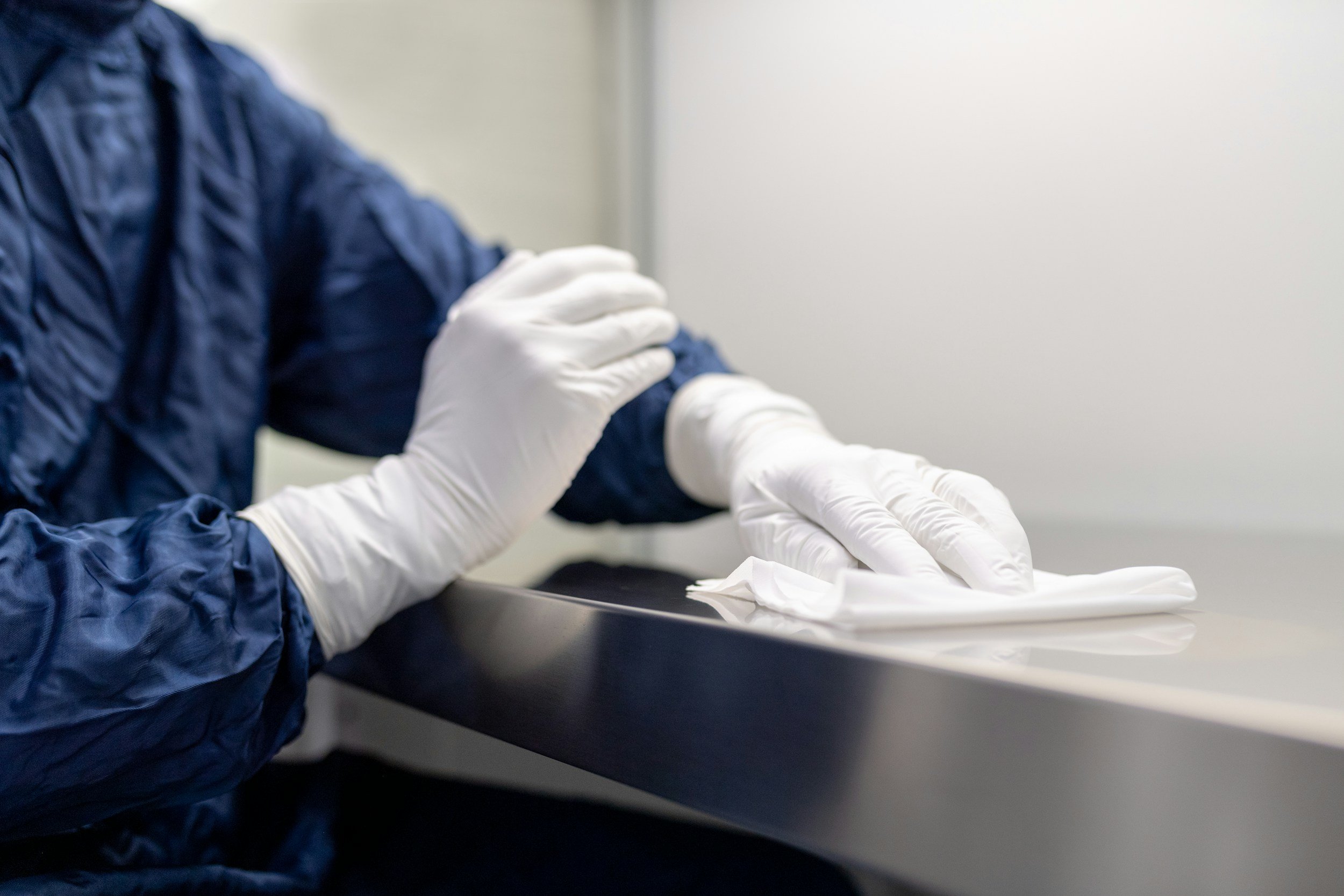 A person wearing a blue jacket and white gloves appears to be administering a shot or injection into another person's arm, who is also wearing a white glove. The scene looks like a healthcare or medical setting.