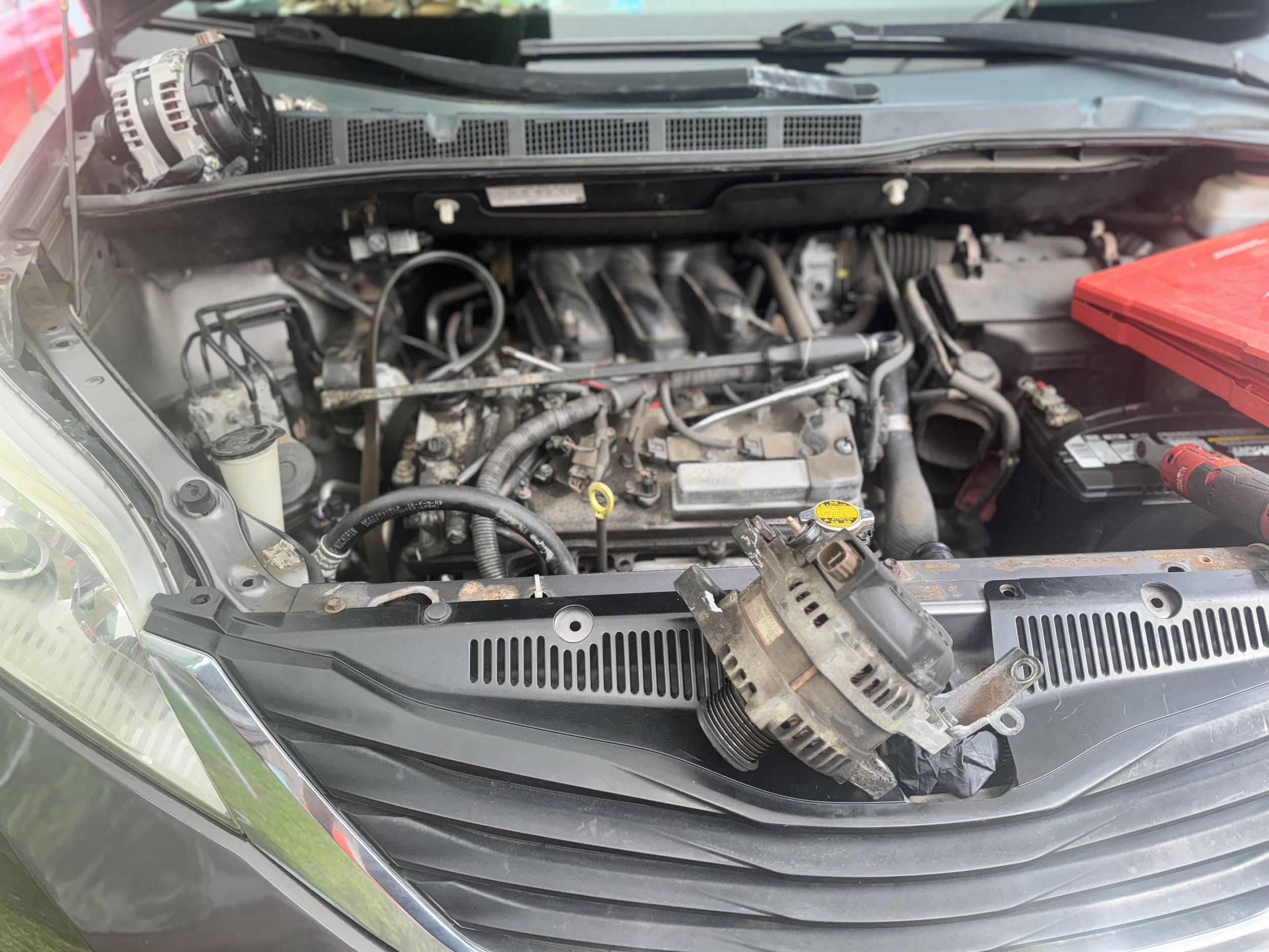Car engine compartment with removed serpentine belt and various engine parts visible.