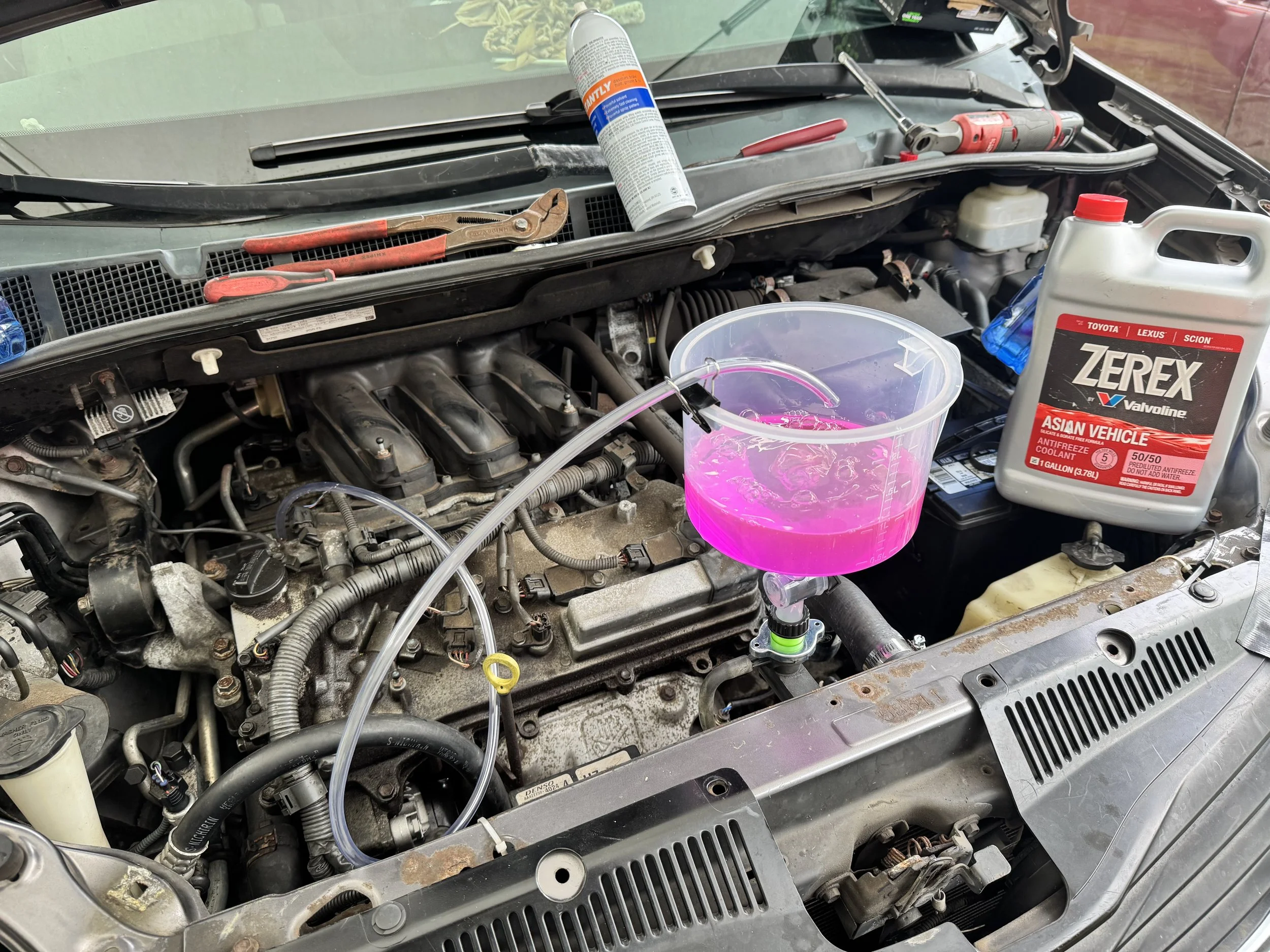 Car hood open with tools and coolant being flushed into the engine.