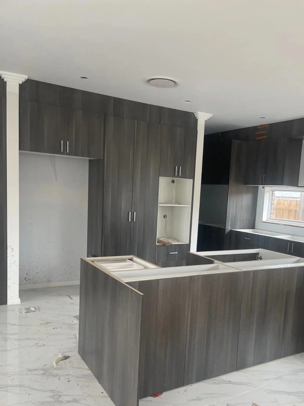 Kitchen under construction with dark wood cabinets, white walls, and a marble floor.