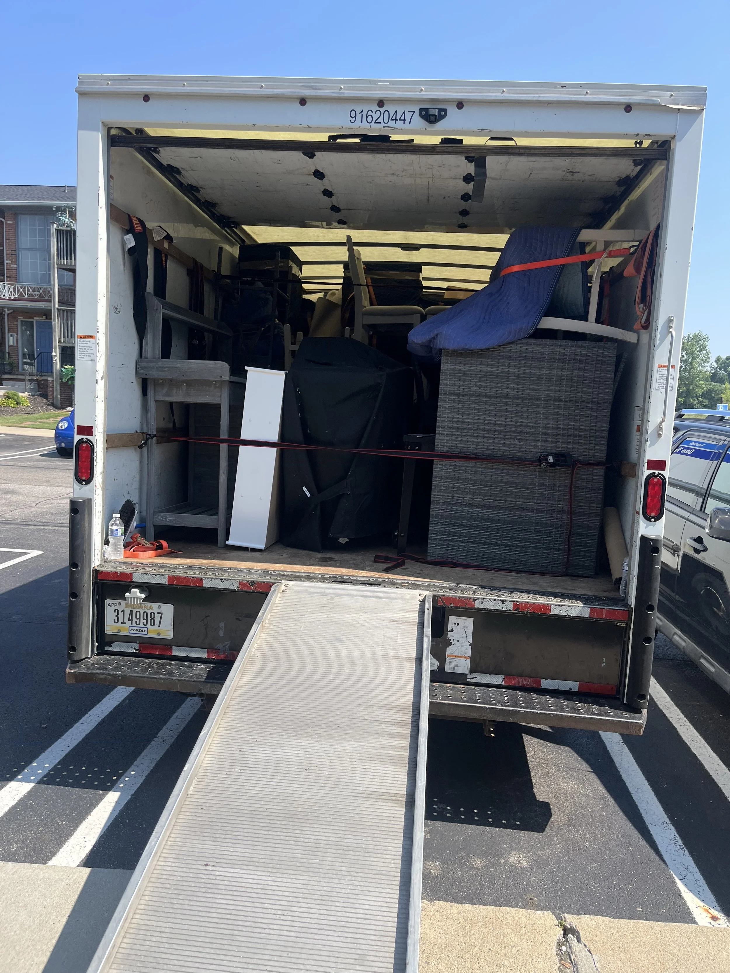 Back of a moving truck with furniture and boxes loaded inside, and a ramp extended to the ground.