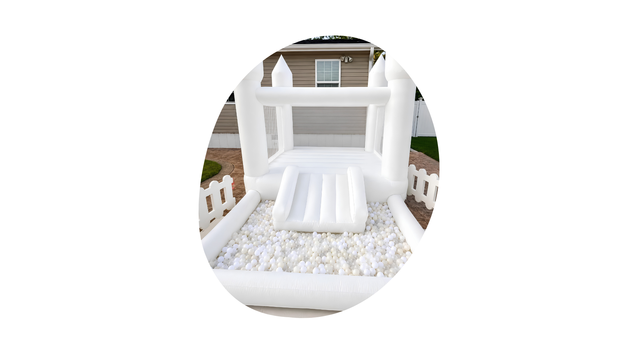 Inflatable white bounce house with a slide, located in a backyard with a brick pathway and a grassy yard. There's a house with tan siding and white trim in the background.