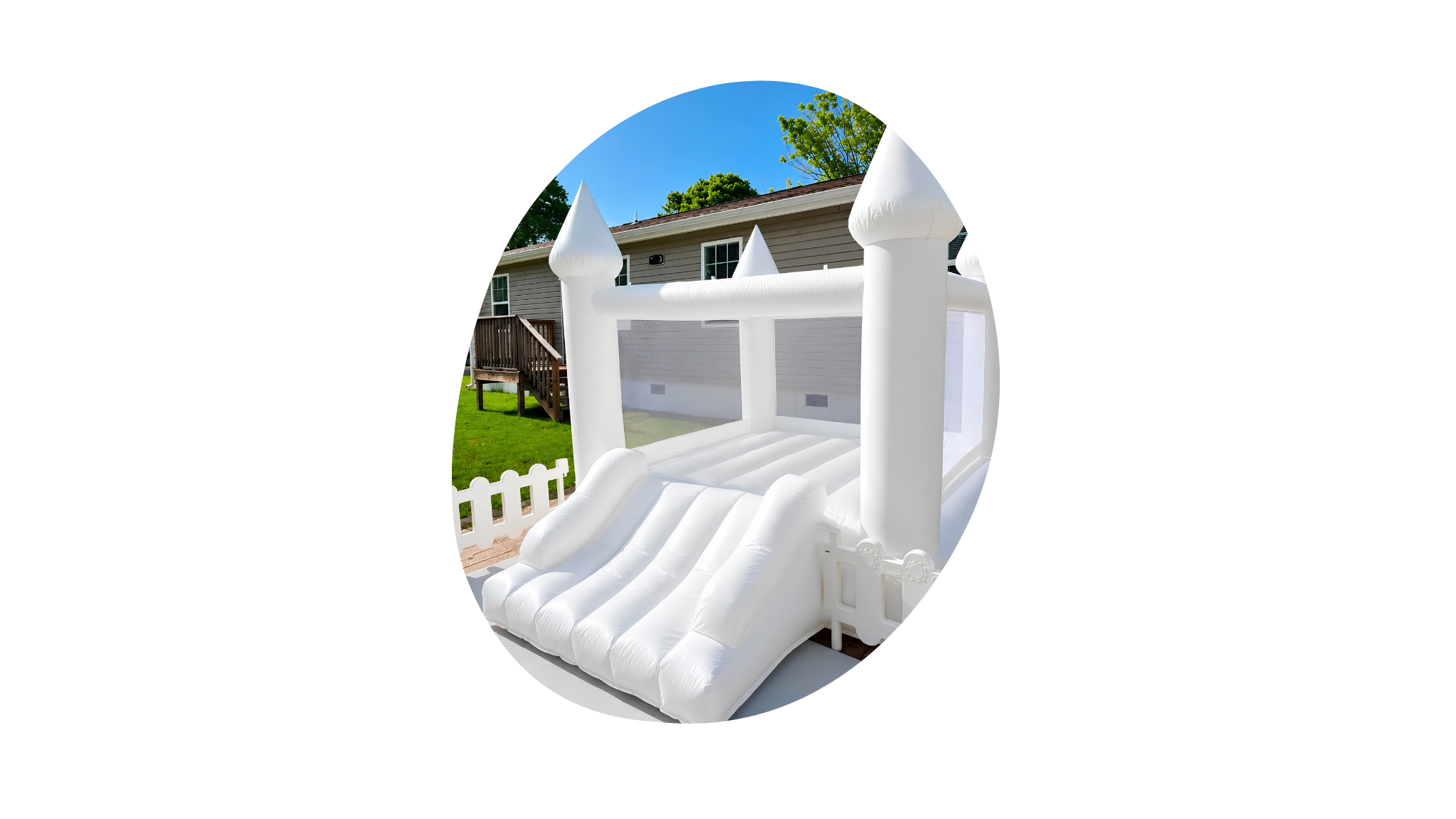 White inflatable bounce house slide with towers, set up in a backyard with a house in the background and a wooden staircase.