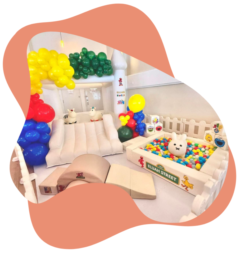 Colorful indoor children's play area with balloon decoration, a small ball pit, stuffed animal toys, and bright cartoon-themed decorations.