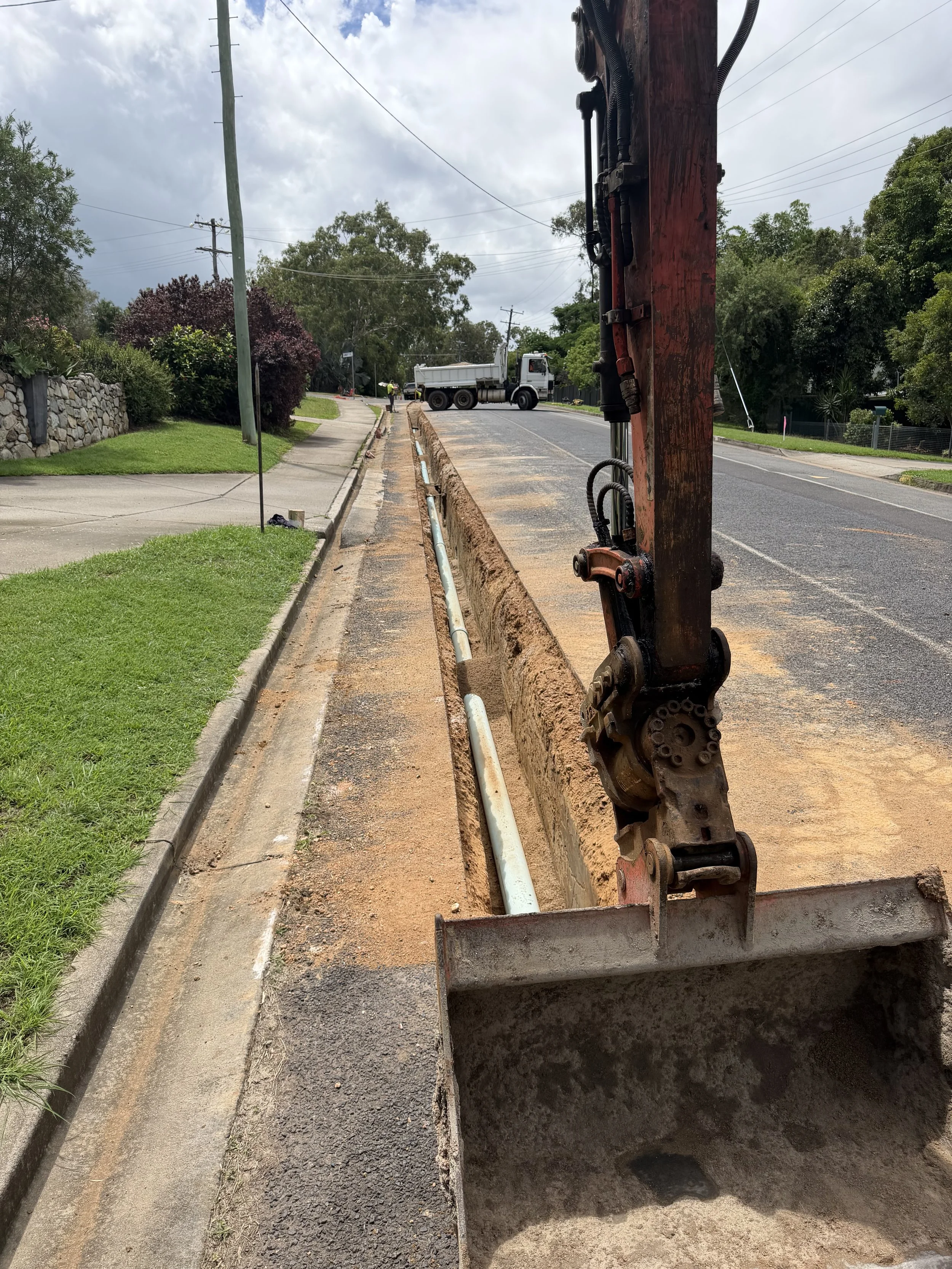 Excavator trenching and installing underground water infrastructure along a suburban roadway in Far North Queensland