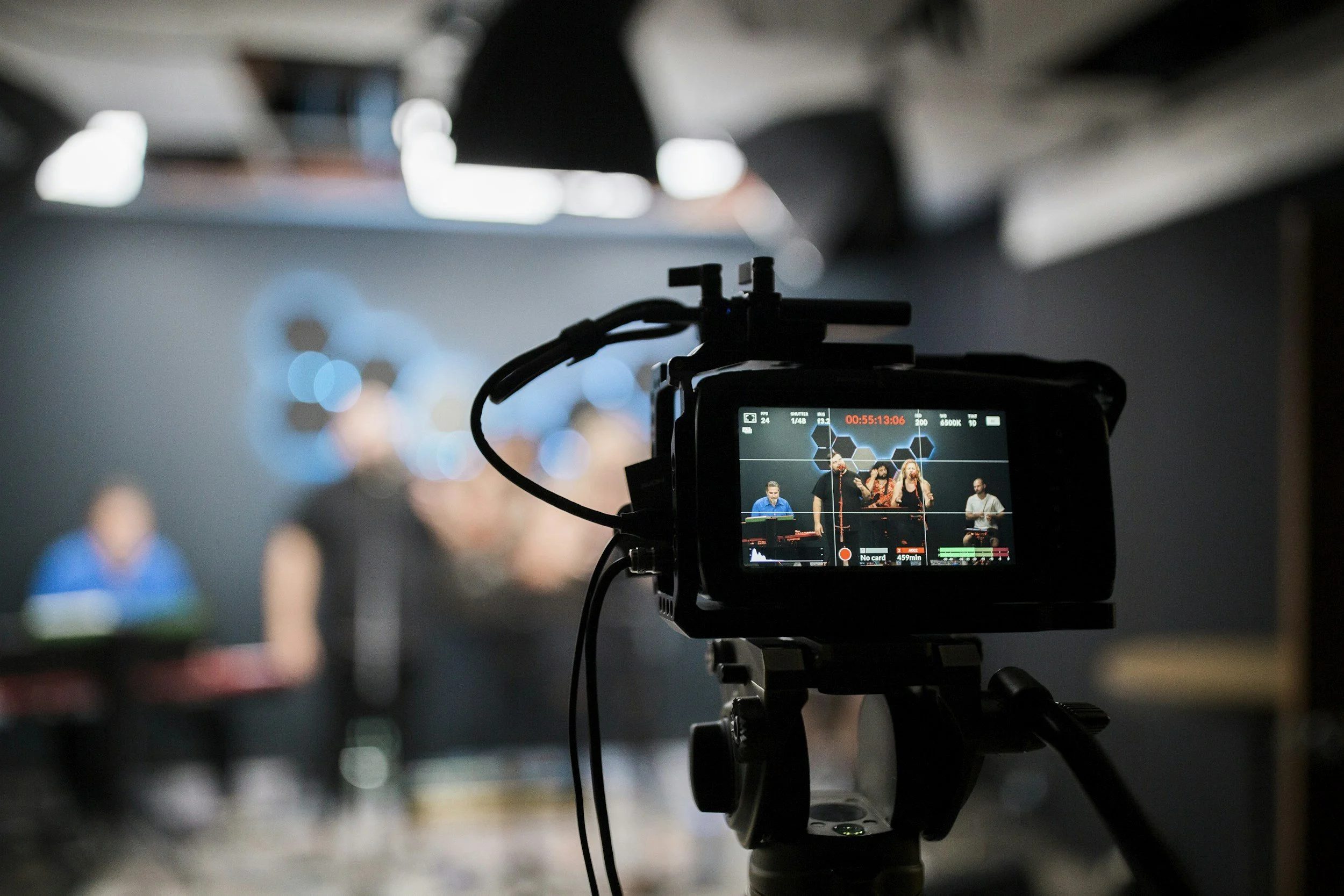 A professional video camera setup recording a performance on a stage with blurred background of performers.