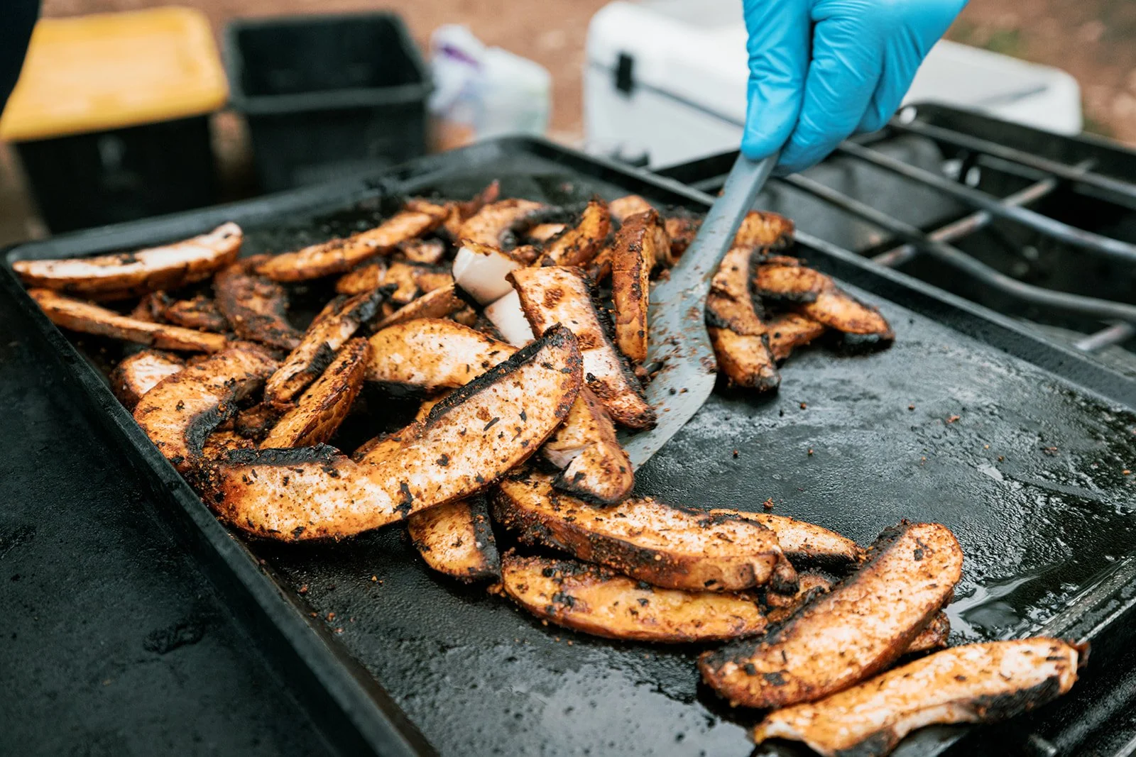 Grilled sausage and chicken strips on a flat-top grill with a person flipping them using tongs.