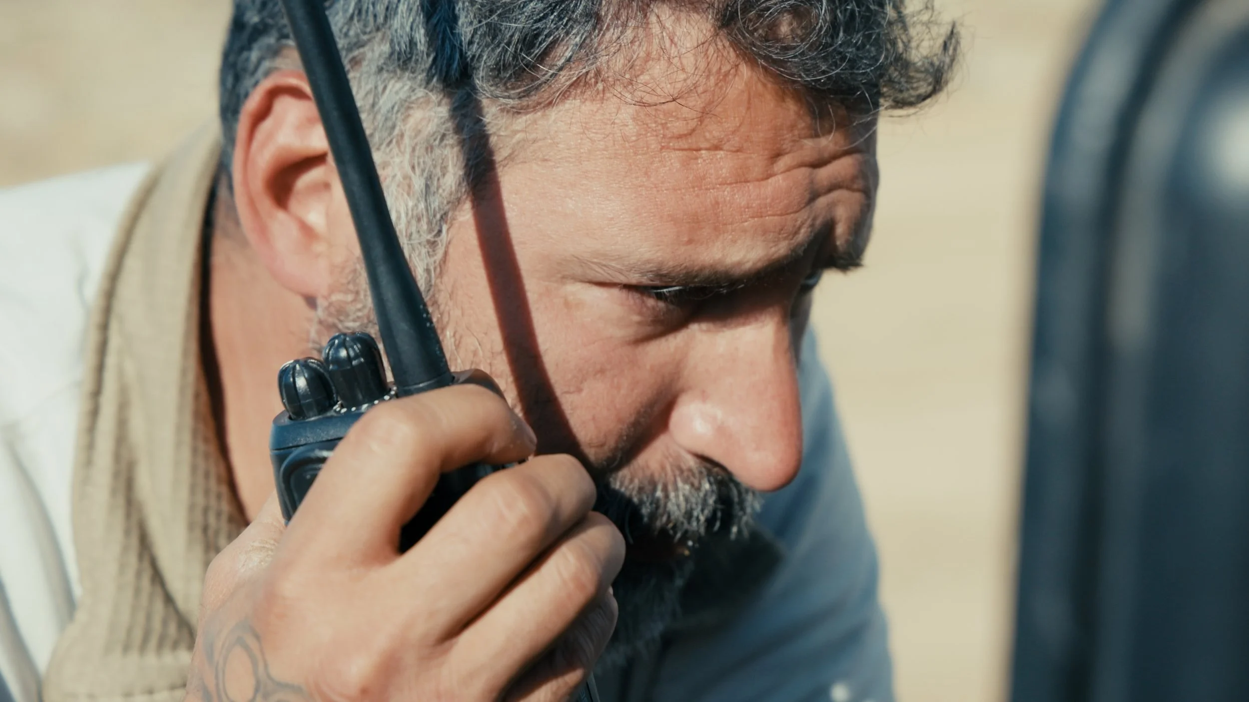 A man with gray hair and a beard talking on a walkie-talkie.