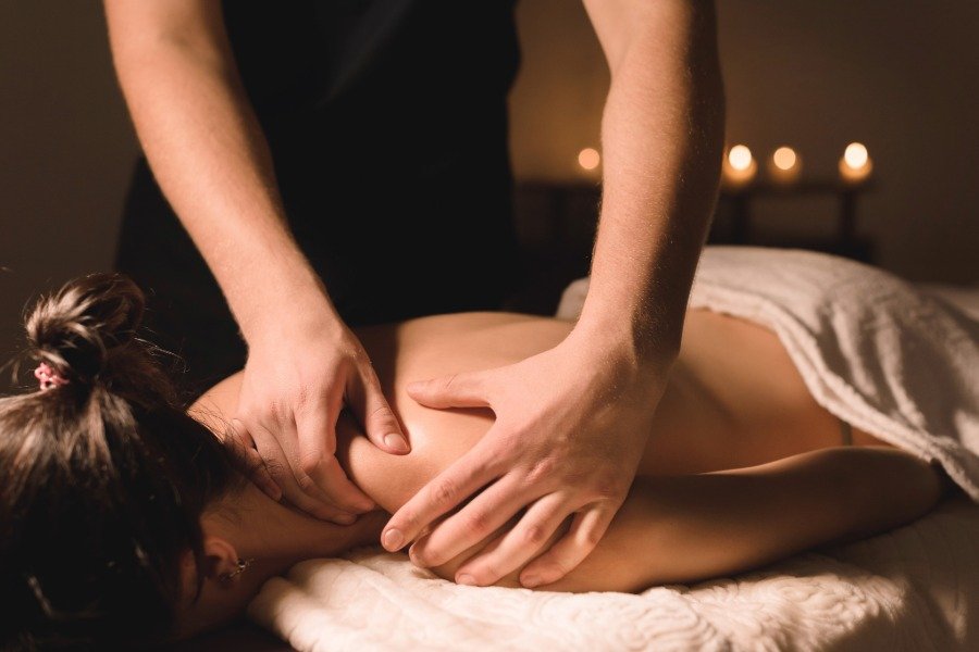 A person receiving a massage from a massage therapist in a dimly lit room with candles on a table in the background