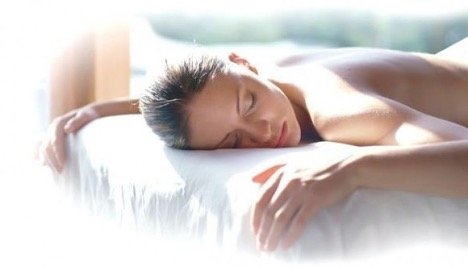 A woman with her eyes closed, lying on her stomach on a bed, receiving a massage.