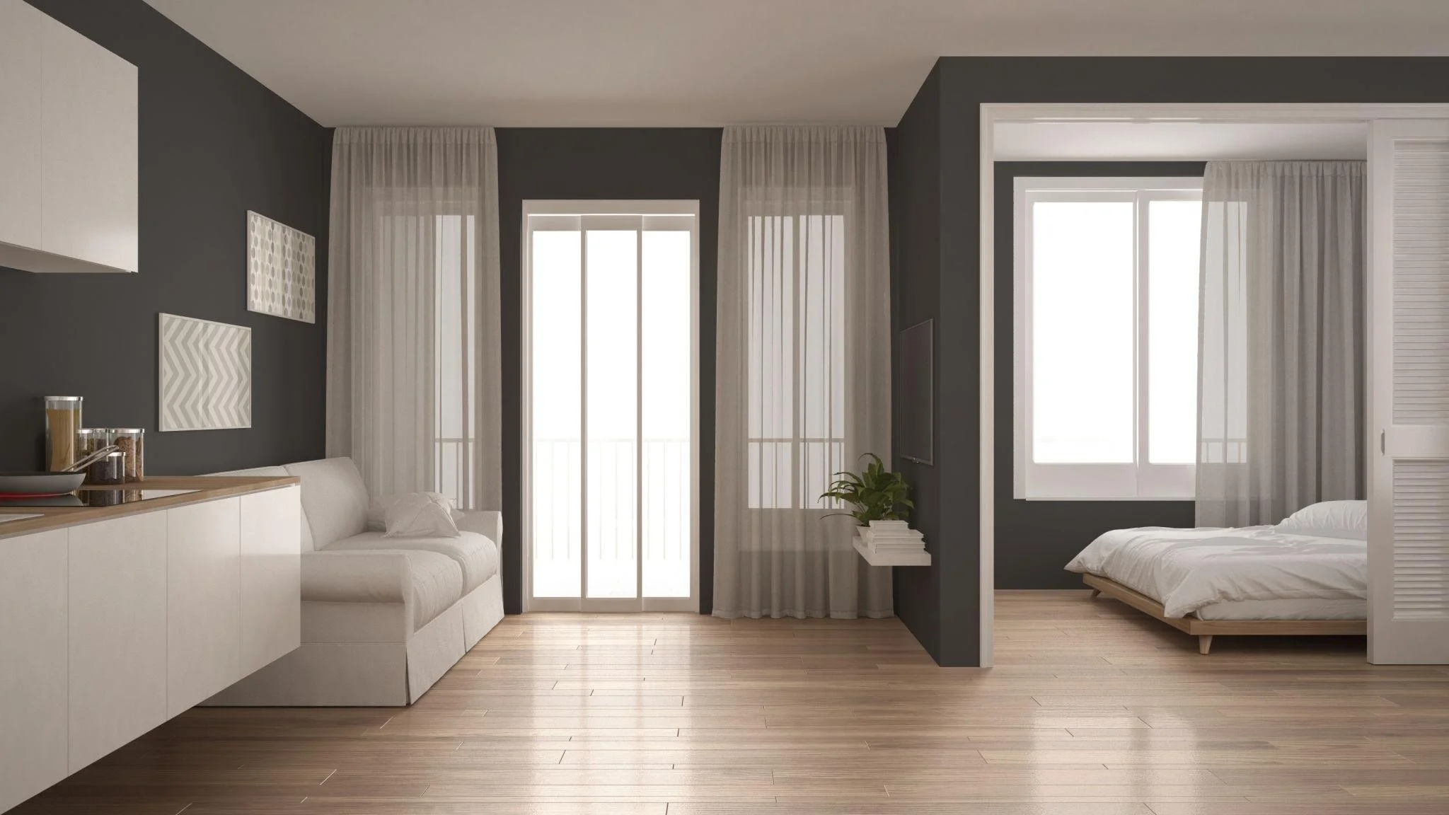 A modern living space with a kitchen area and a bedroom separated by a black wall. The room has wooden flooring, large windows with sheer curtains, and minimalist decor, including framed artwork and a potted plant.