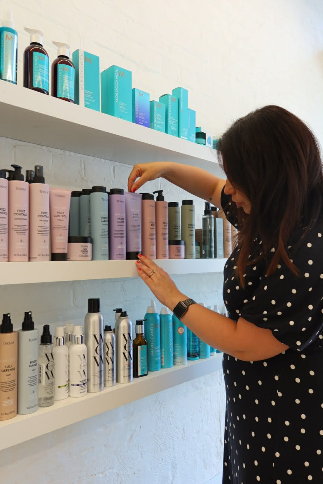 Woman selecting hair care products on shelves in a store.