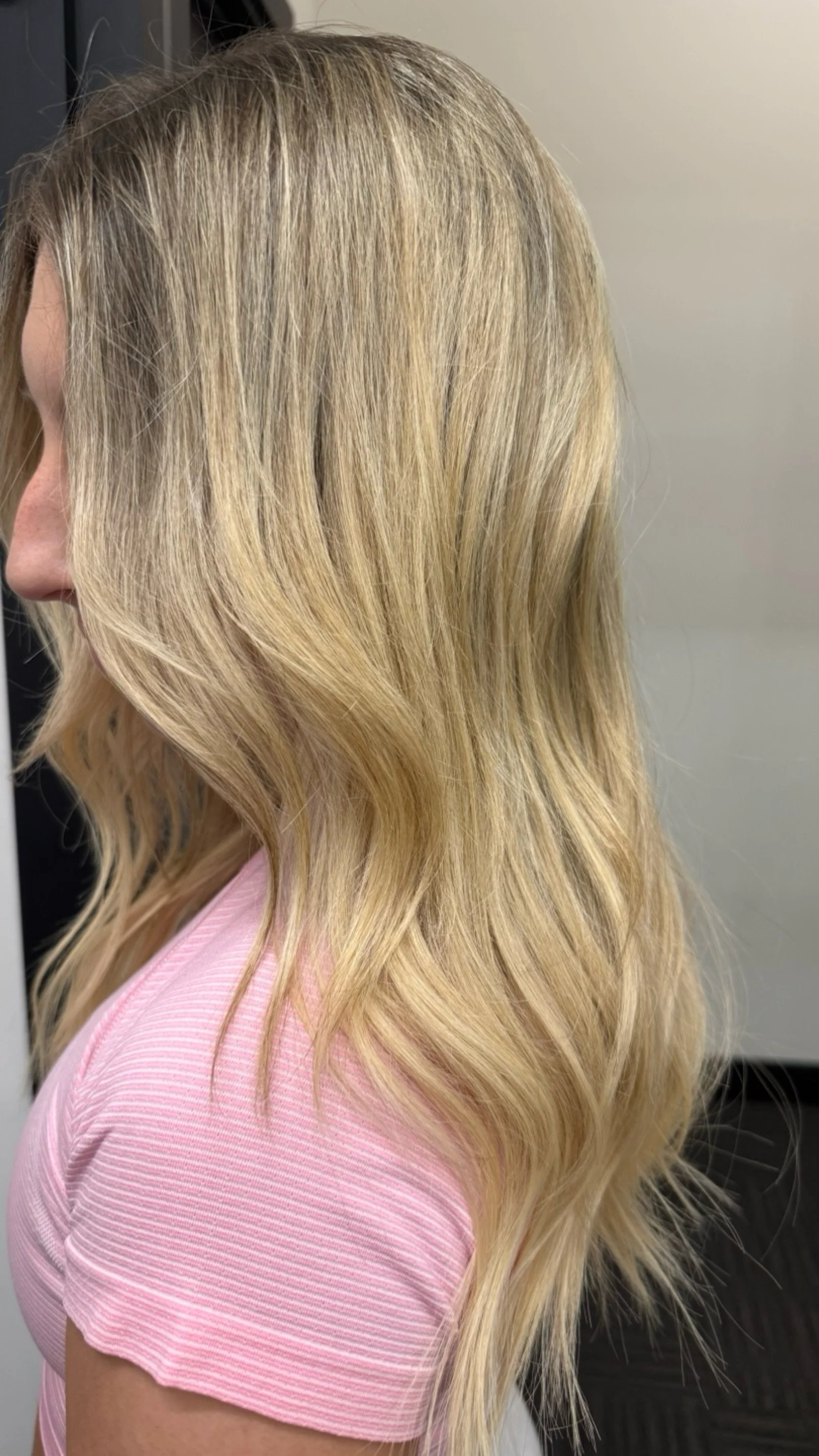 Profile view of a woman with long, wavy blonde hair wearing a pink top.