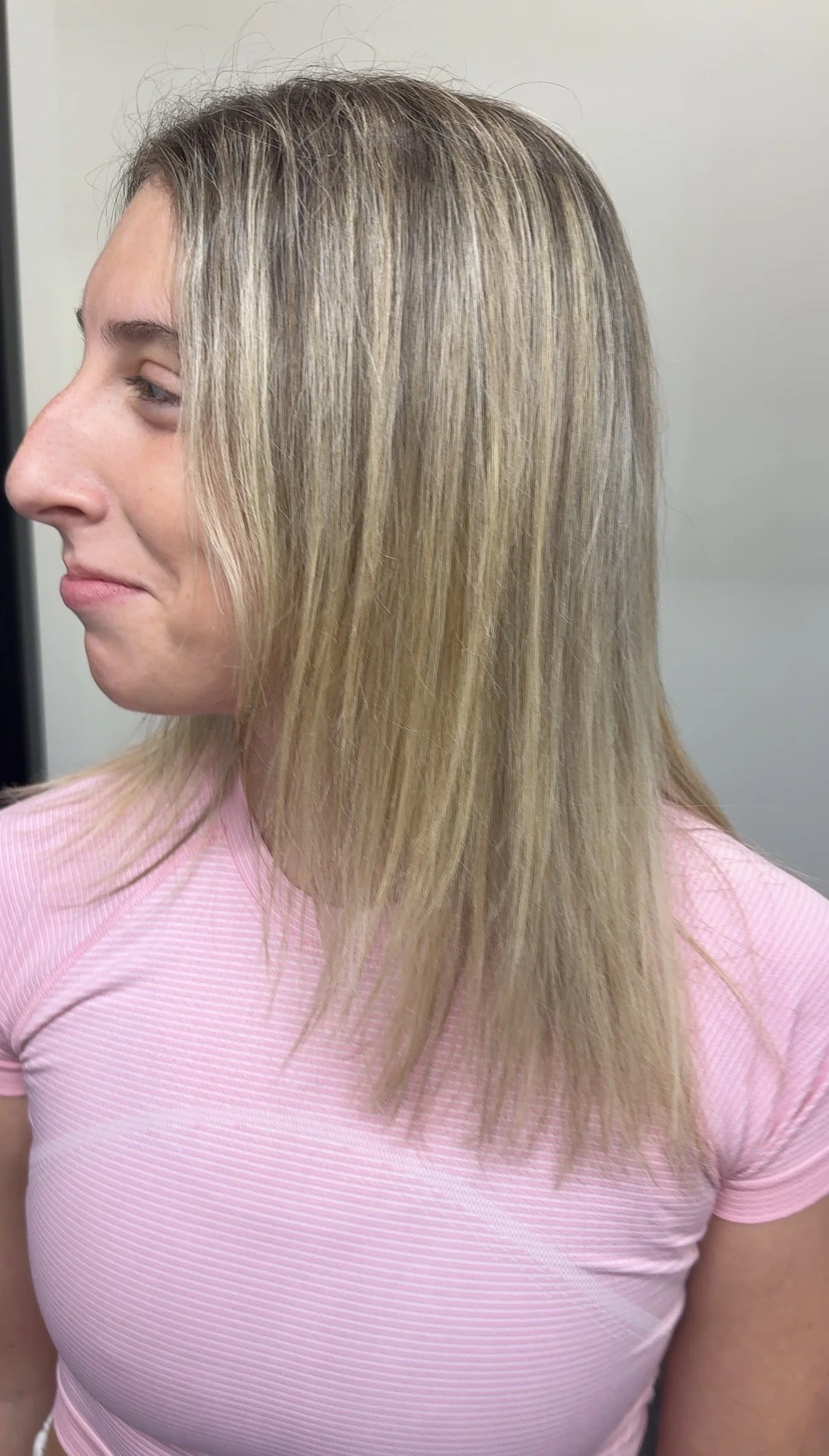 A woman with straight, blonde hair wearing a pink ribbed shirt, facing left against a plain background.
