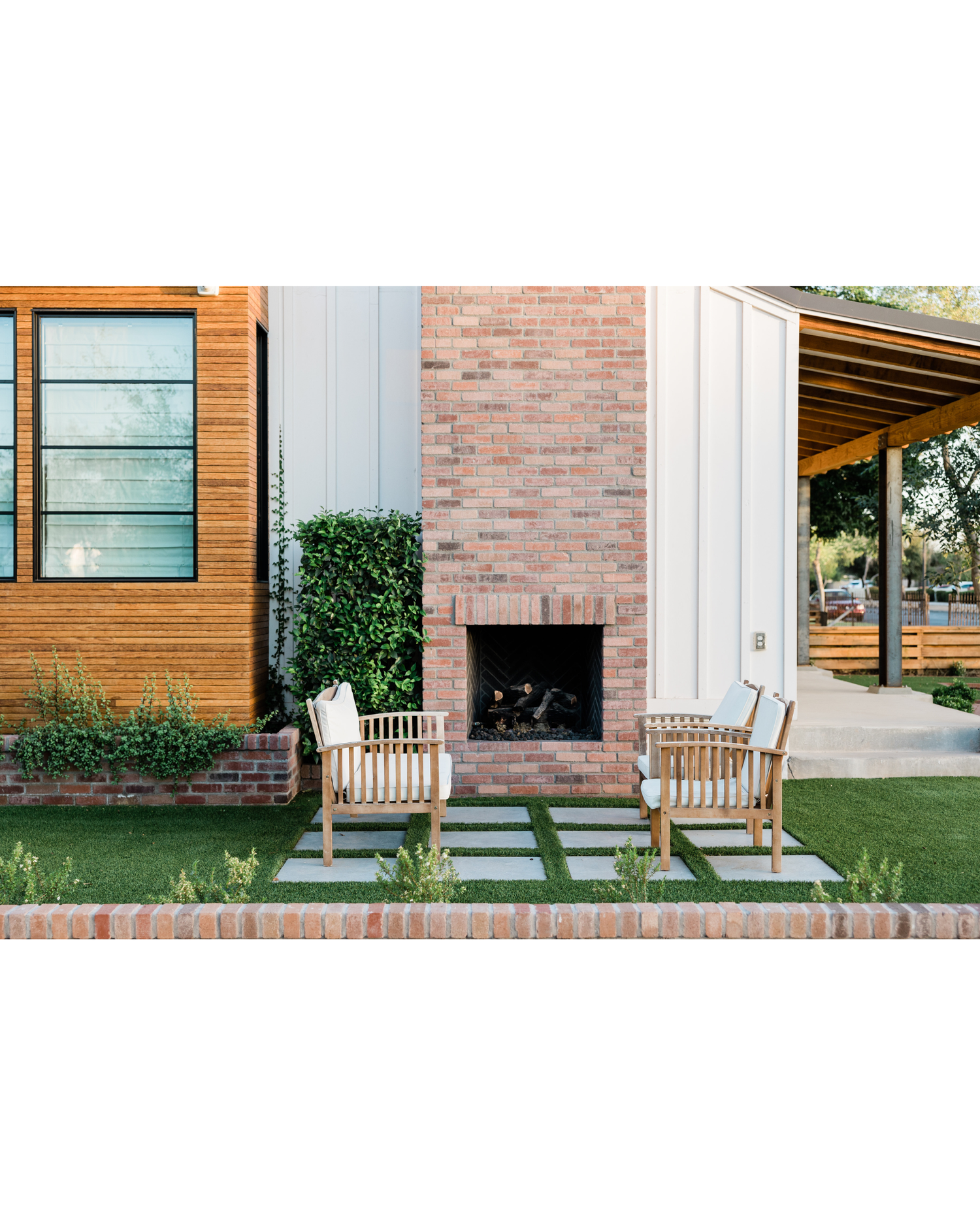 Modern house exterior with brick, wood, and metal siding, large window, outdoor fireplace, patio chairs, and manicured landscaping in Northern Colorado