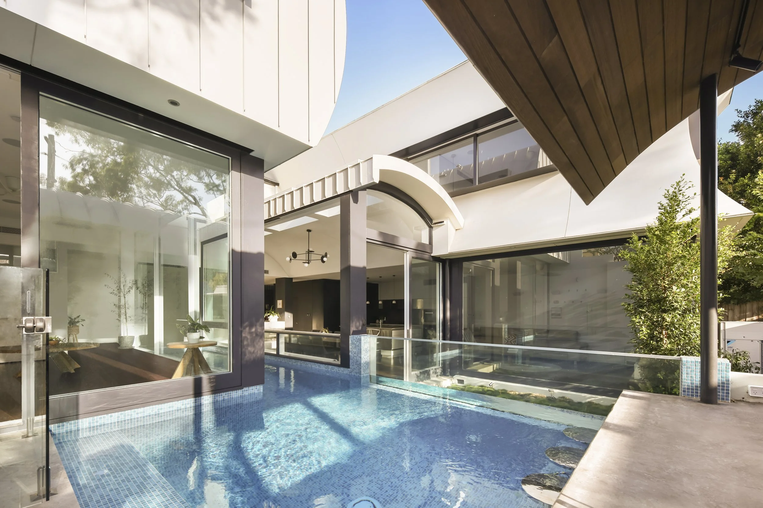 Modern house with large glass windows and doors, a swimming pool, and wooden and white exterior architectural elements under a clear blue sky.