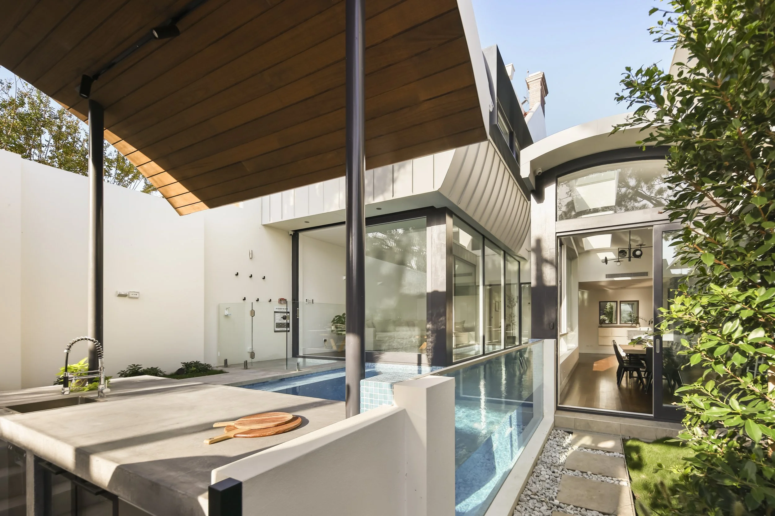 Modern house with curved roof, large glass windows, pool, outdoor seating, and lush greenery.