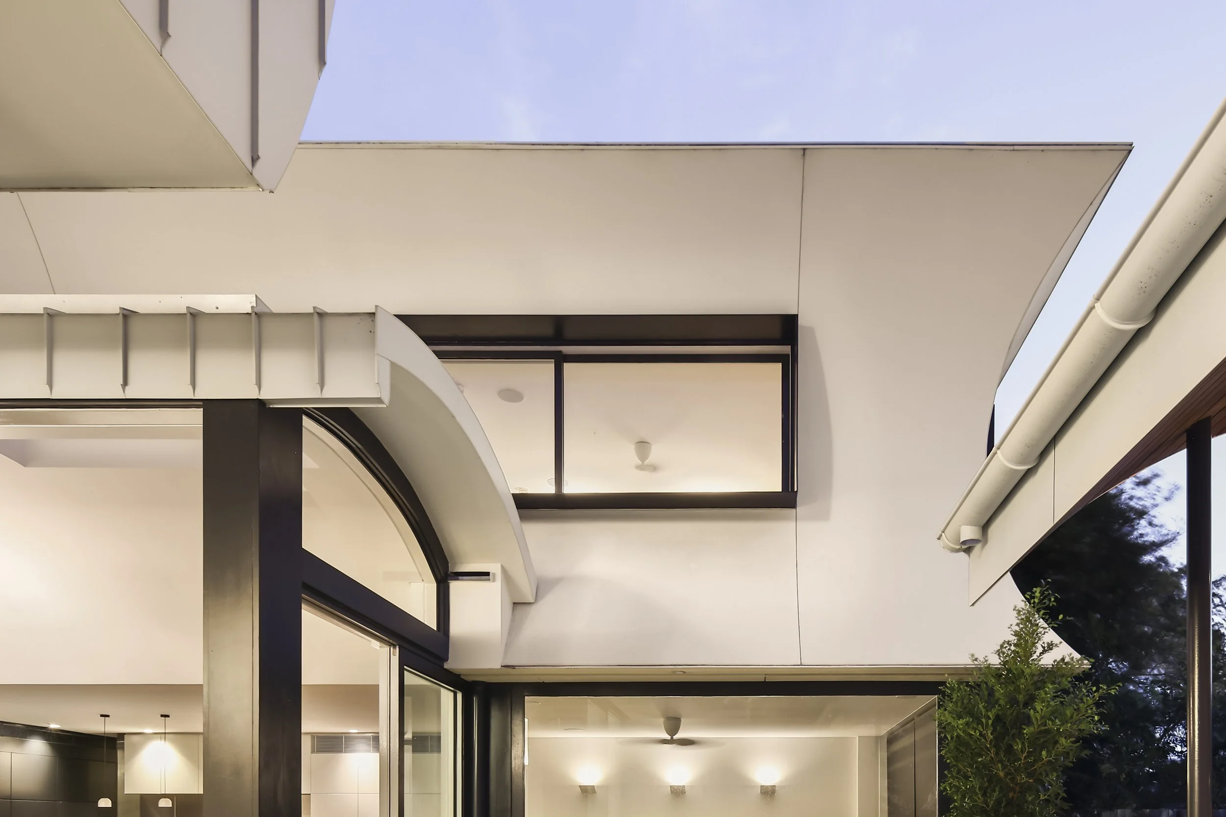 Modern building exterior with white overhangs, black metal frames, large glass doors, and a potted tree outside.