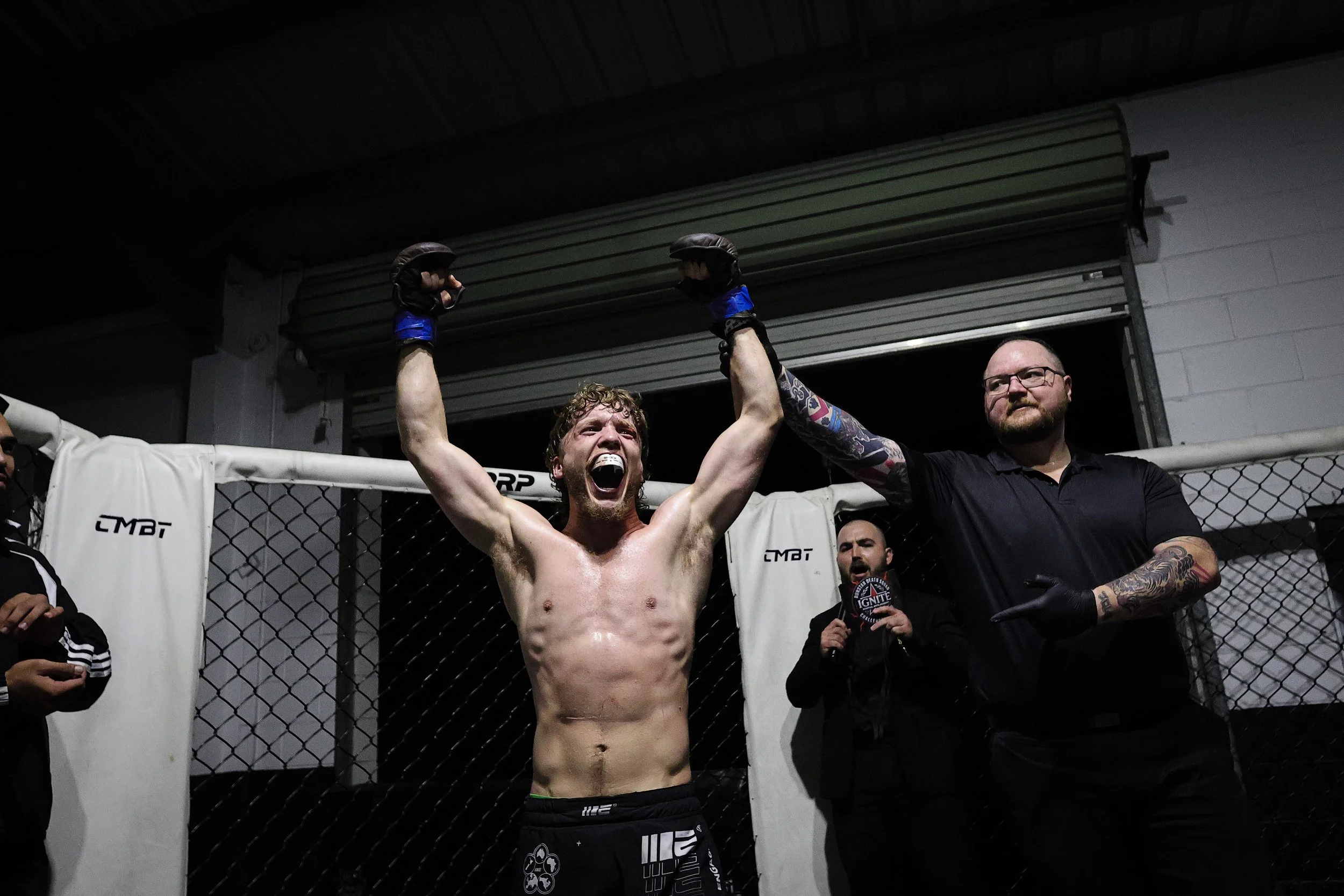 Mixed martial arts fighter celebrating victory inside an octagon cage, with a man raising his hand in triumph and a referee next to them.