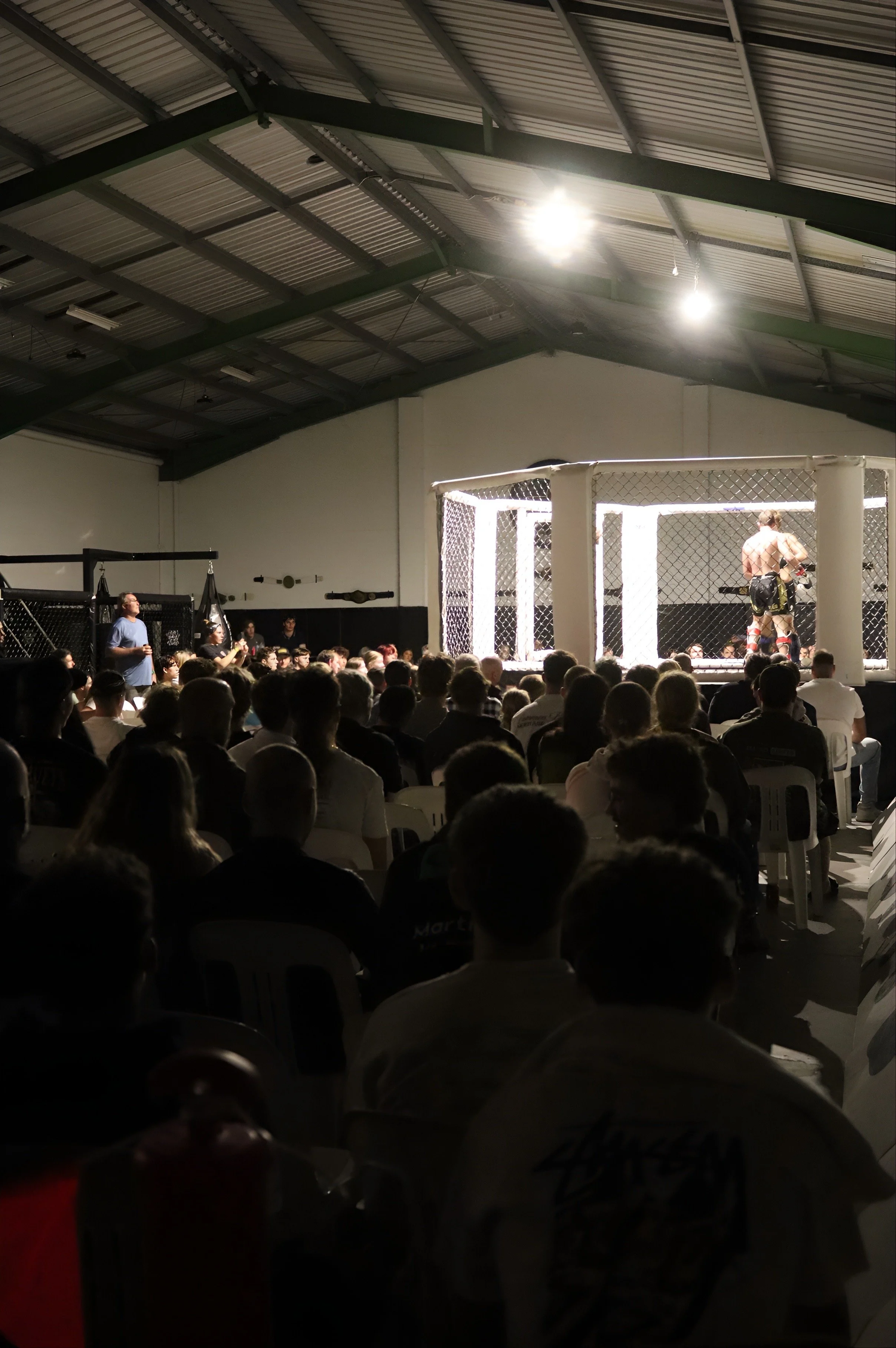 Mixed martial arts fight inside an octagon-shaped cage with spectators seated around watching the fighters.