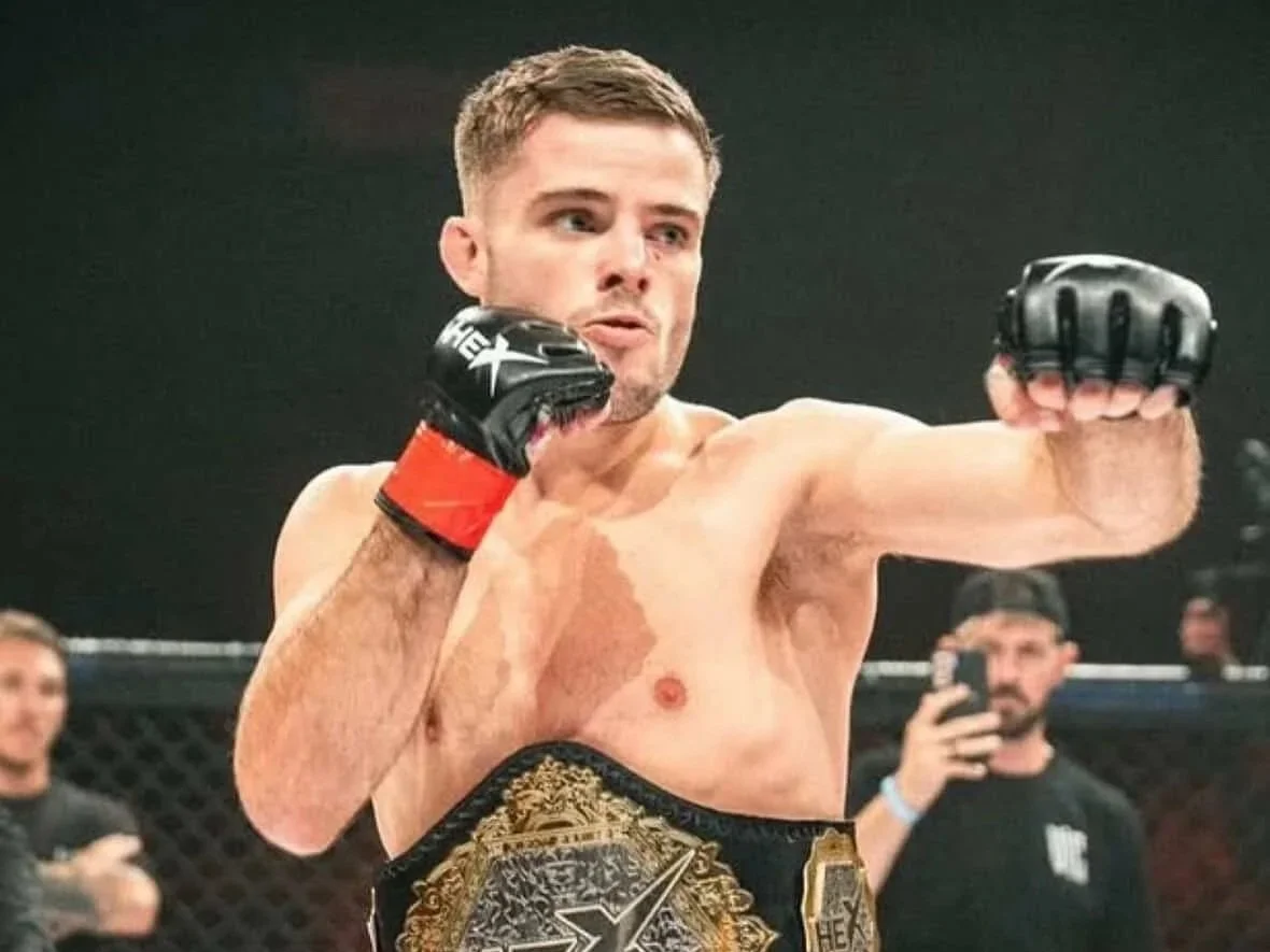 Mixed martial arts fighter with championship belt around his waist, wearing gloves, throwing a punch.