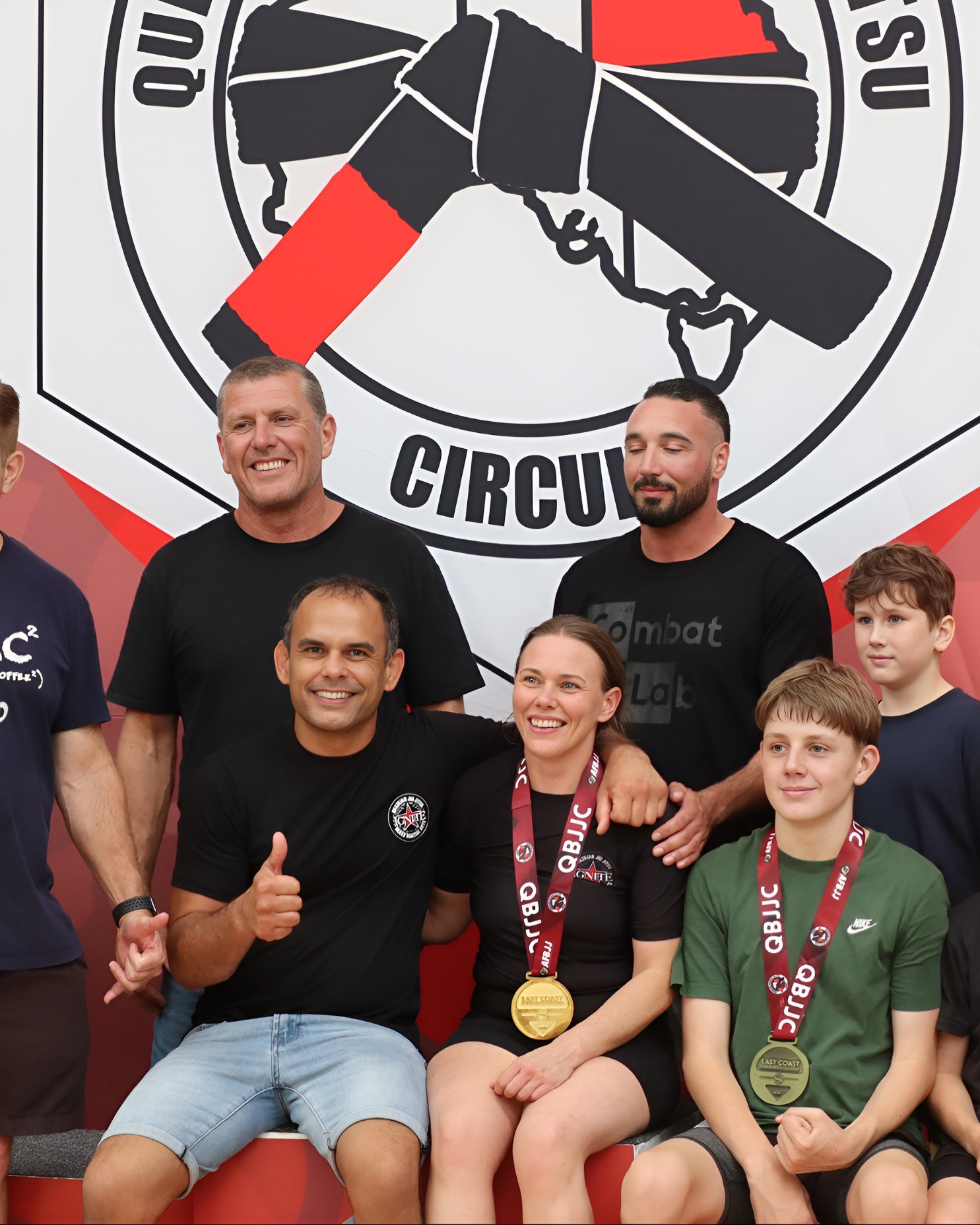 A group of people posing at a podium. Competition team regularly competes with high success. Two individuals are wearing medals around their necks, indicating a competition or race event. The group appears happy and celebratory.