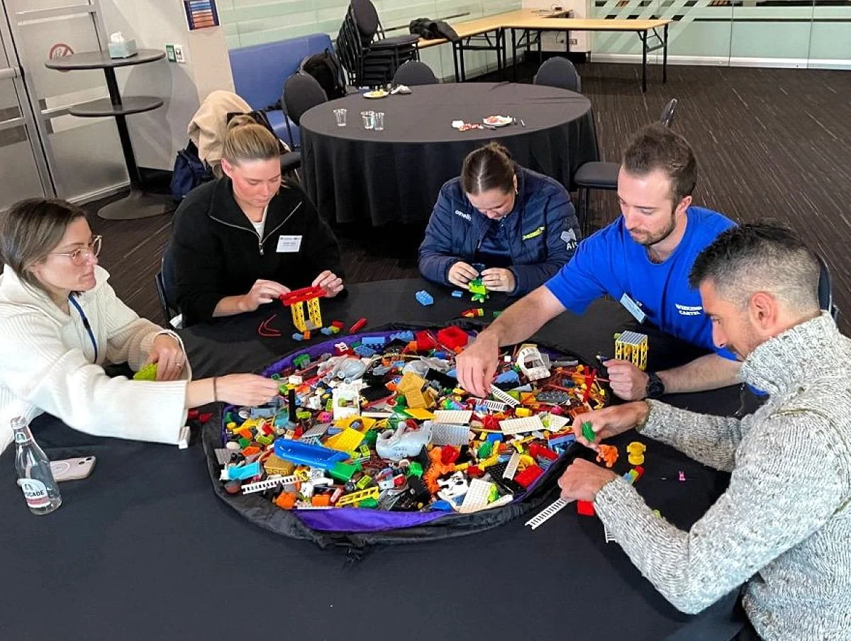 Five people sit at a round table during a 'Lego Serious Play' session delivered by Chris Spinks during a team development day.
