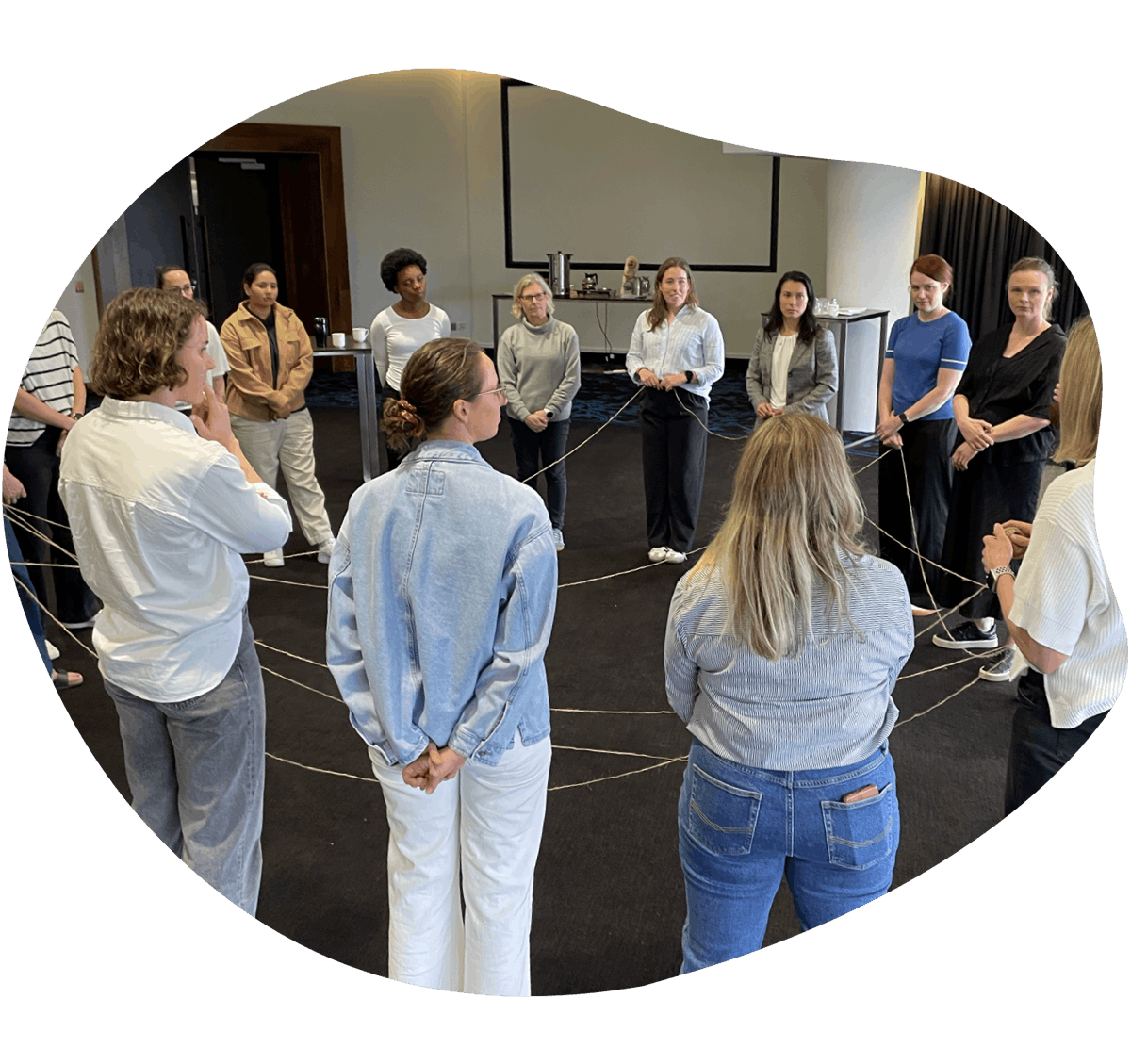 A photo during a Nobis workshop using string and group exercises. Several women stand in a circle connected by the string.
