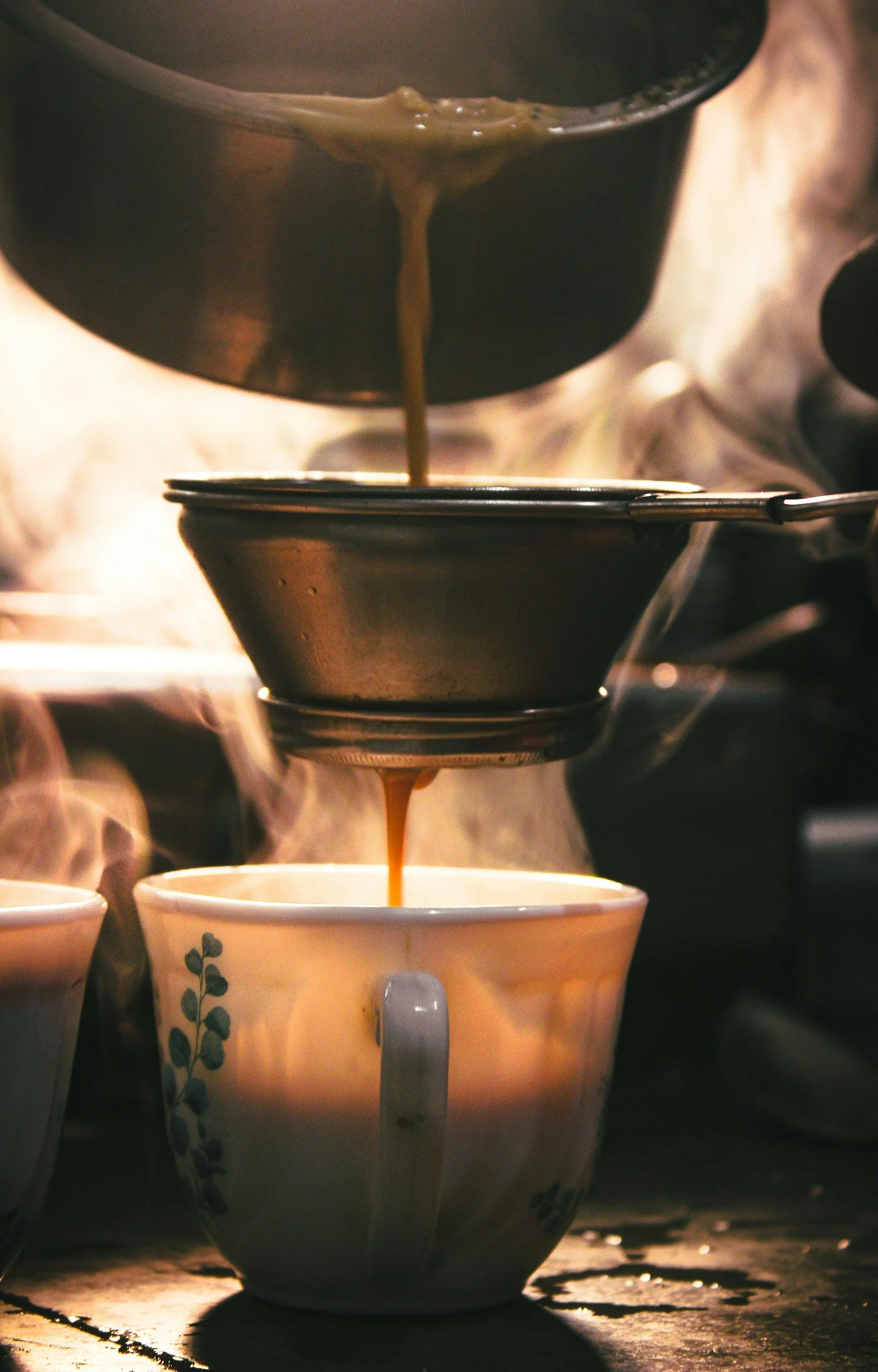 Pouring hot beverage from a pot into a ceramic mug with blue floral design on a rustic wooden surface.