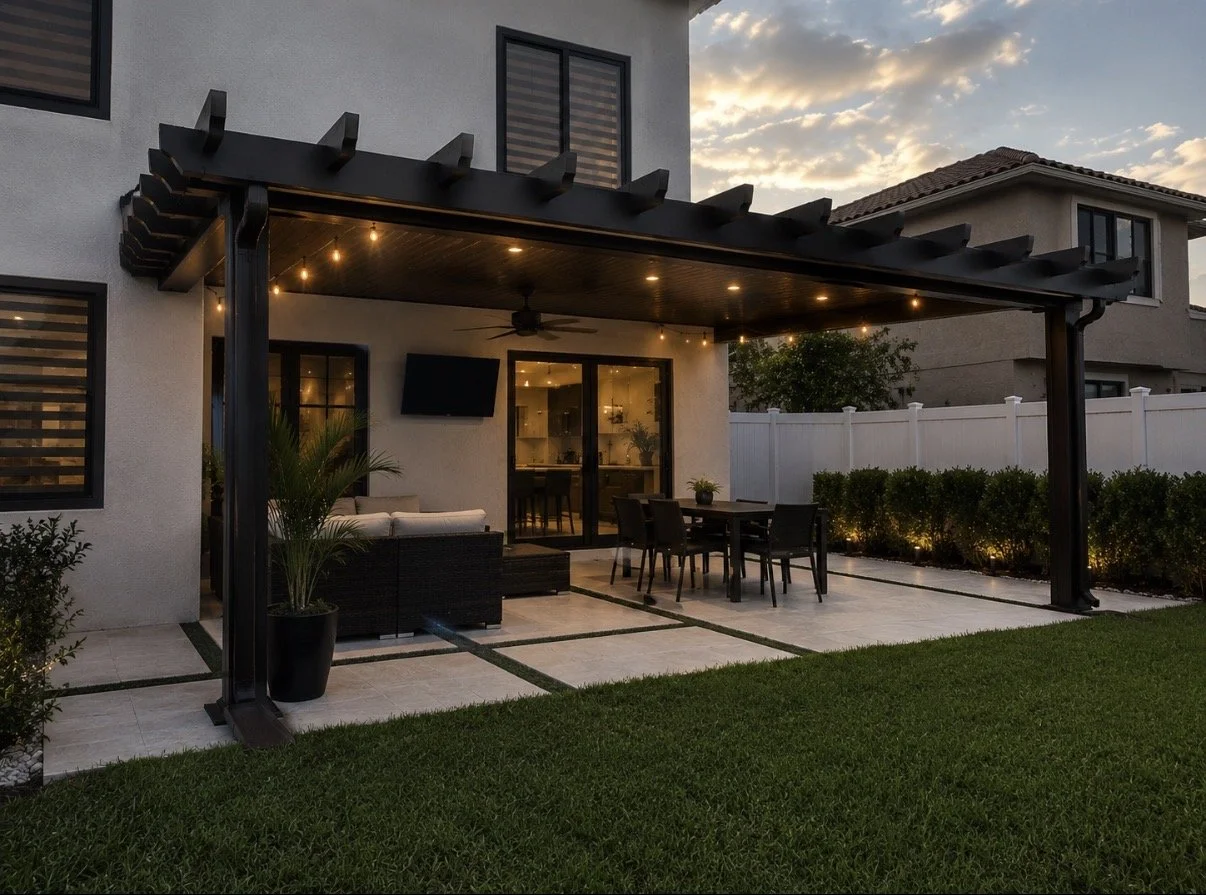 Backyard patio area with outdoor furniture, string lights, and a pergola, with a lawn in the foreground and neighboring houses in the background during sunset.