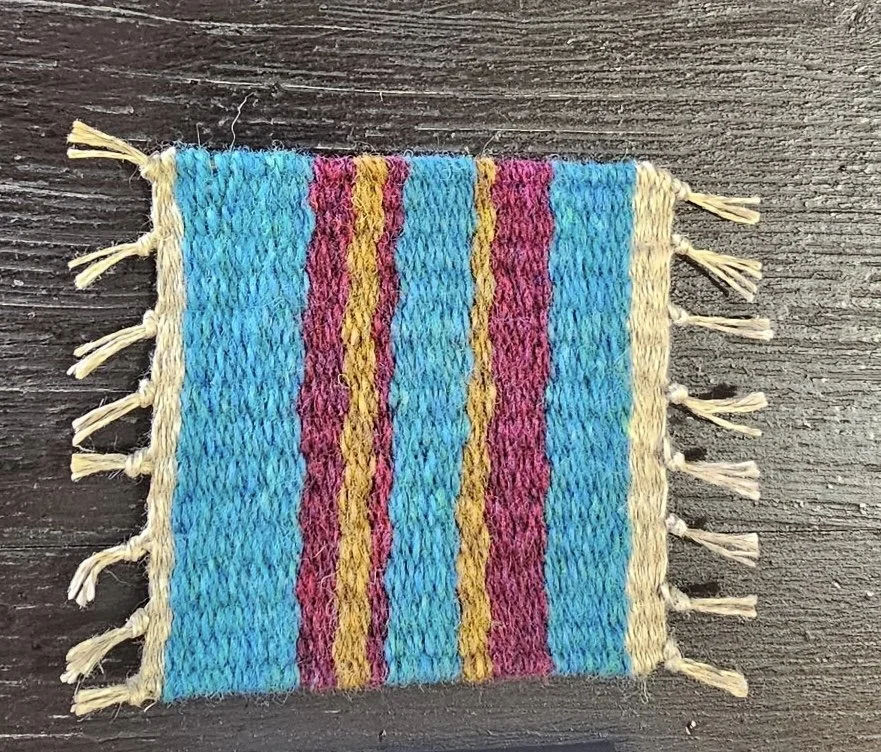 Colorful woven textile with blue, pink, yellow, and cream stripes and tassels on sides, placed on a dark wooden surface.