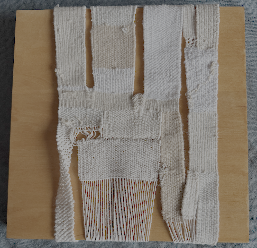 Close-up of a wooden loom weaving white fabric on a tan wooden surface.