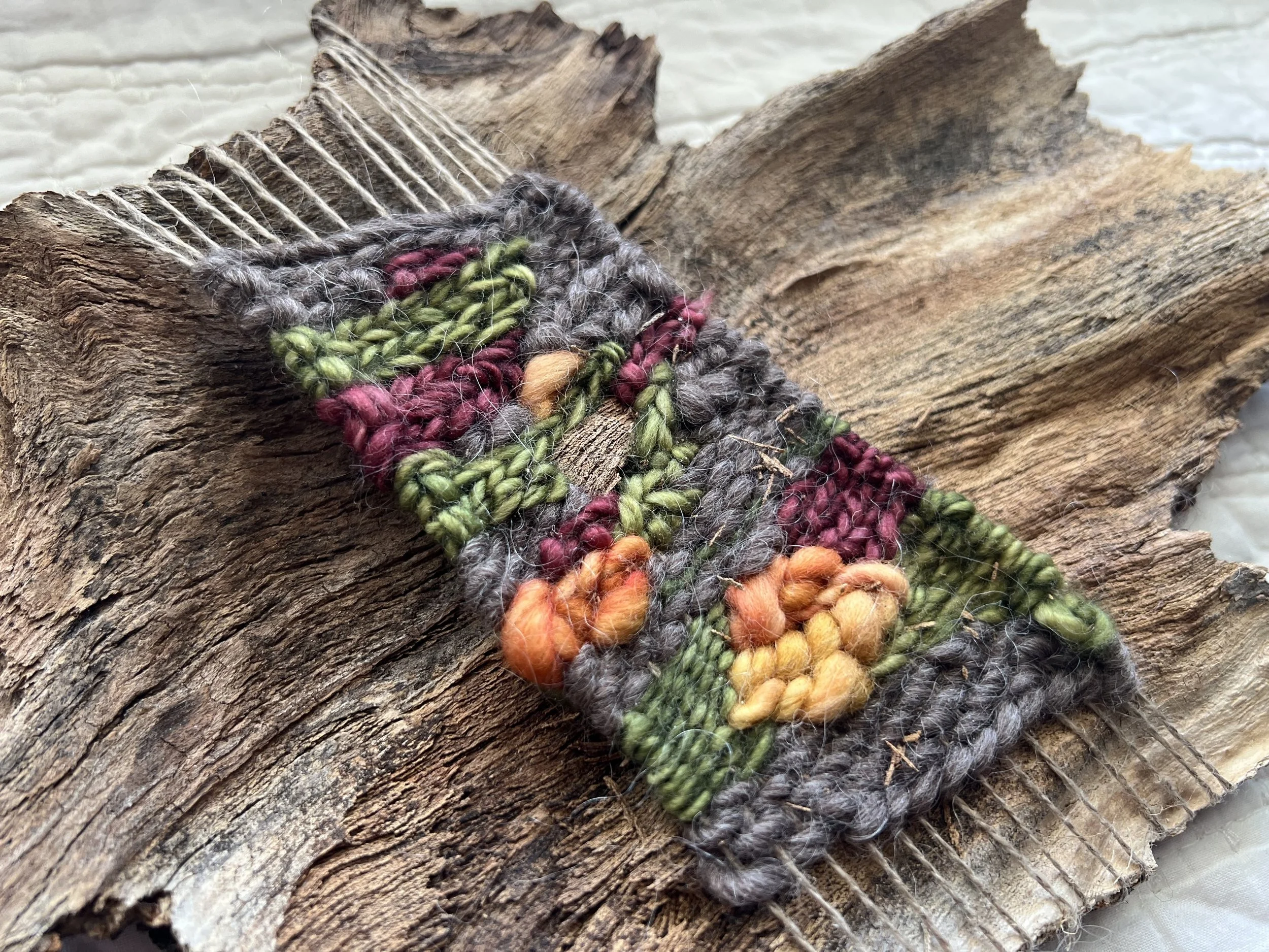 Close-up of colorful, textured yarn woven through a piece of rough, weathered wood against a light background.
