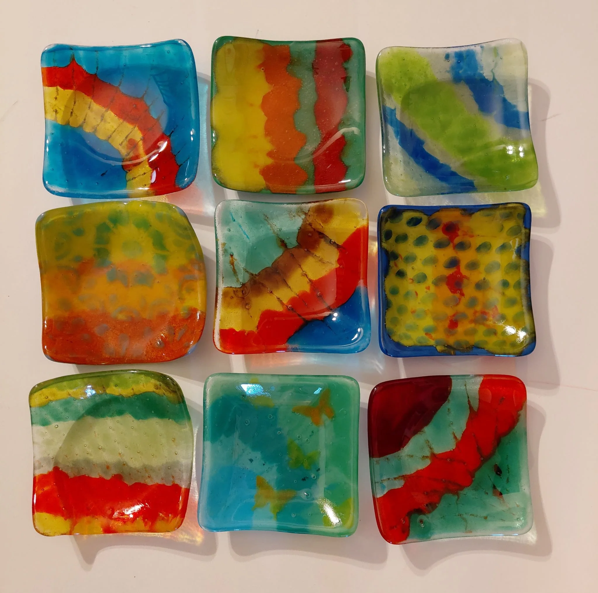 Colorful handmade glass soap dishes with abstract swirl designs in shades of blue, green, red, yellow, and orange.